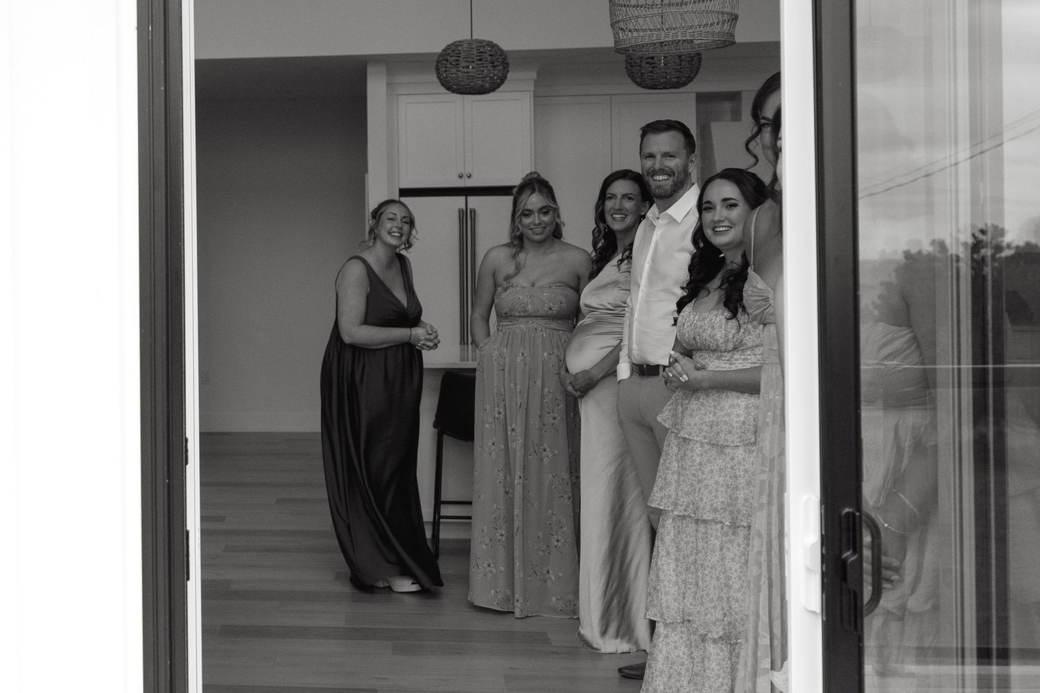 Wedding party poses in front of large windows in a bright modern venue.