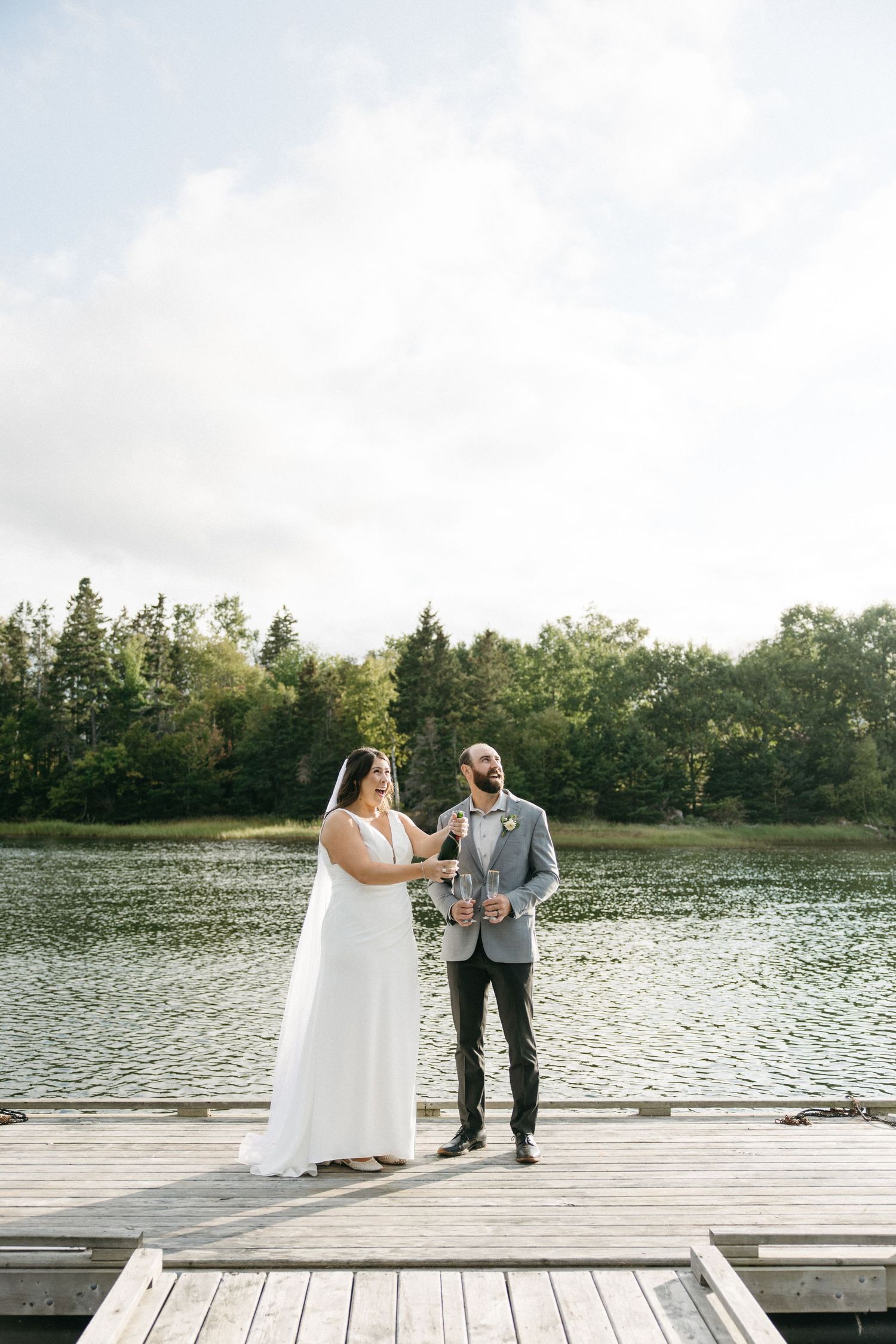 A couple shares a romantic moment on a wooden dock overlooking a serene lake surrounded by trees.