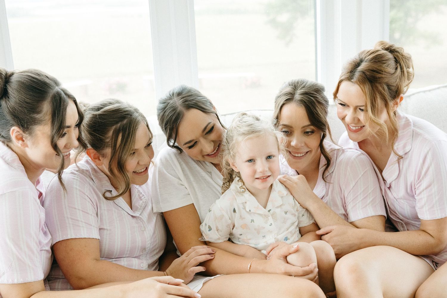 Family members share loving moments together in soft white clothing by a bright window.