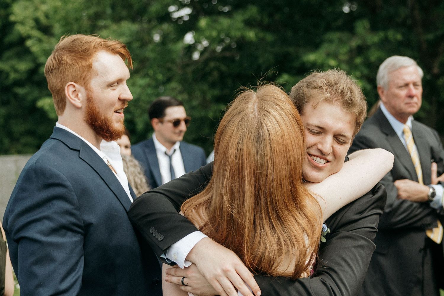 Wedding guests exchange warm hugs during an outdoor reception celebration.