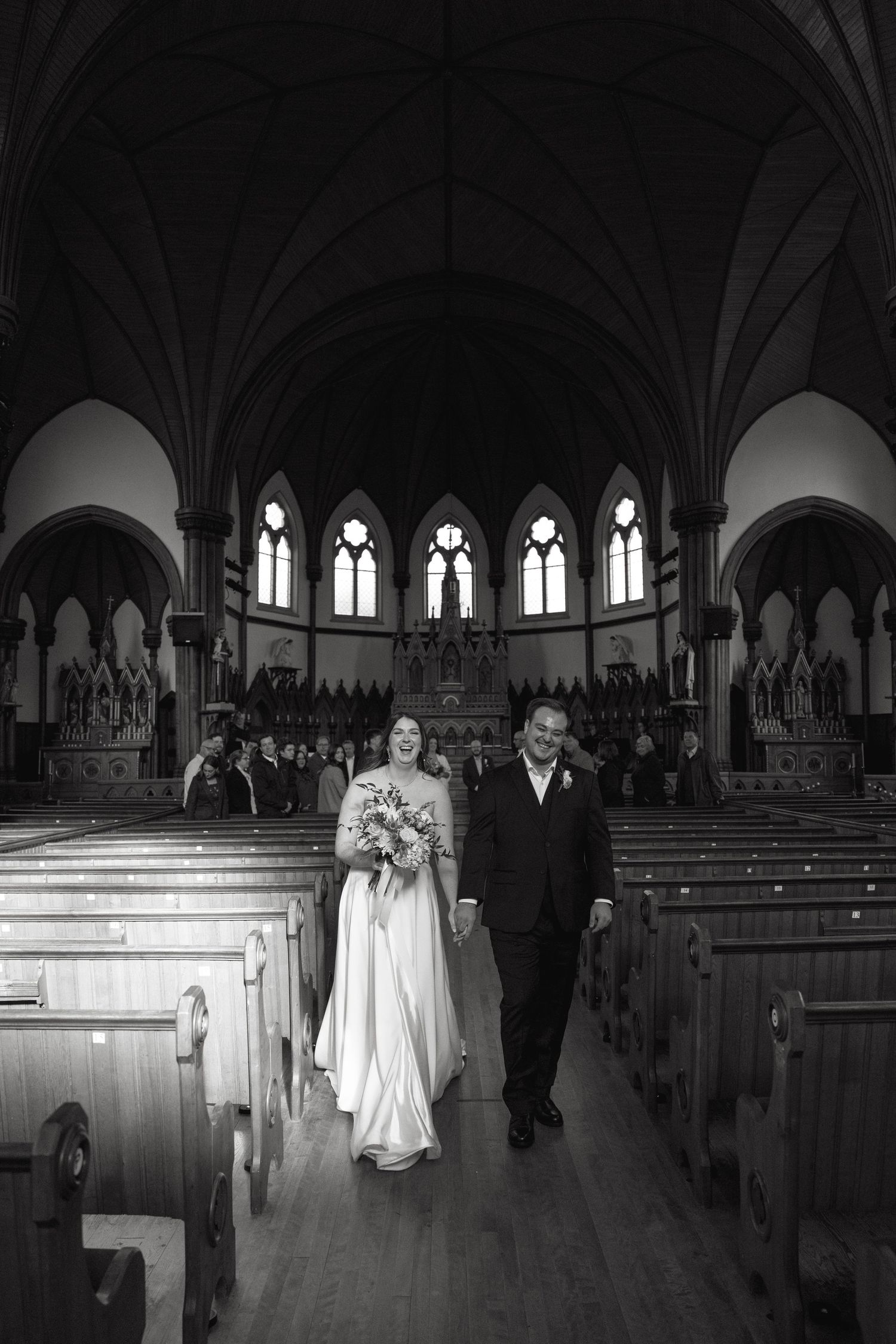 A black and white photograph of a wedding ceremony in a grand cathedral with vaulted ceilings and stained glass windows.