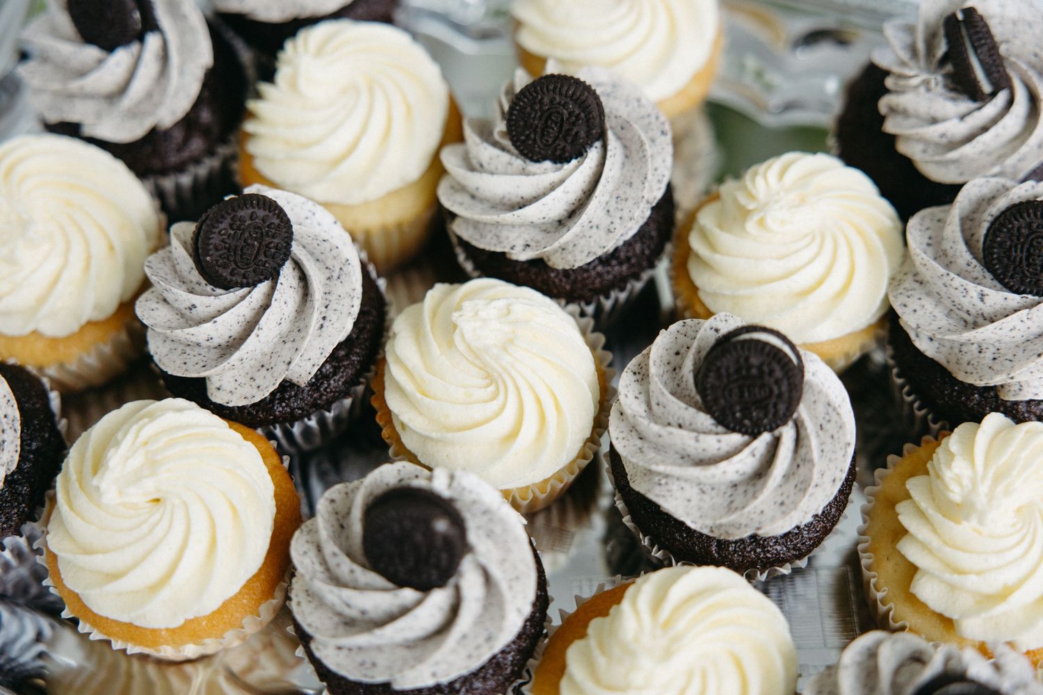 Assorted wedding cupcakes with white vanilla and Oreo frosting displayed on a platter.