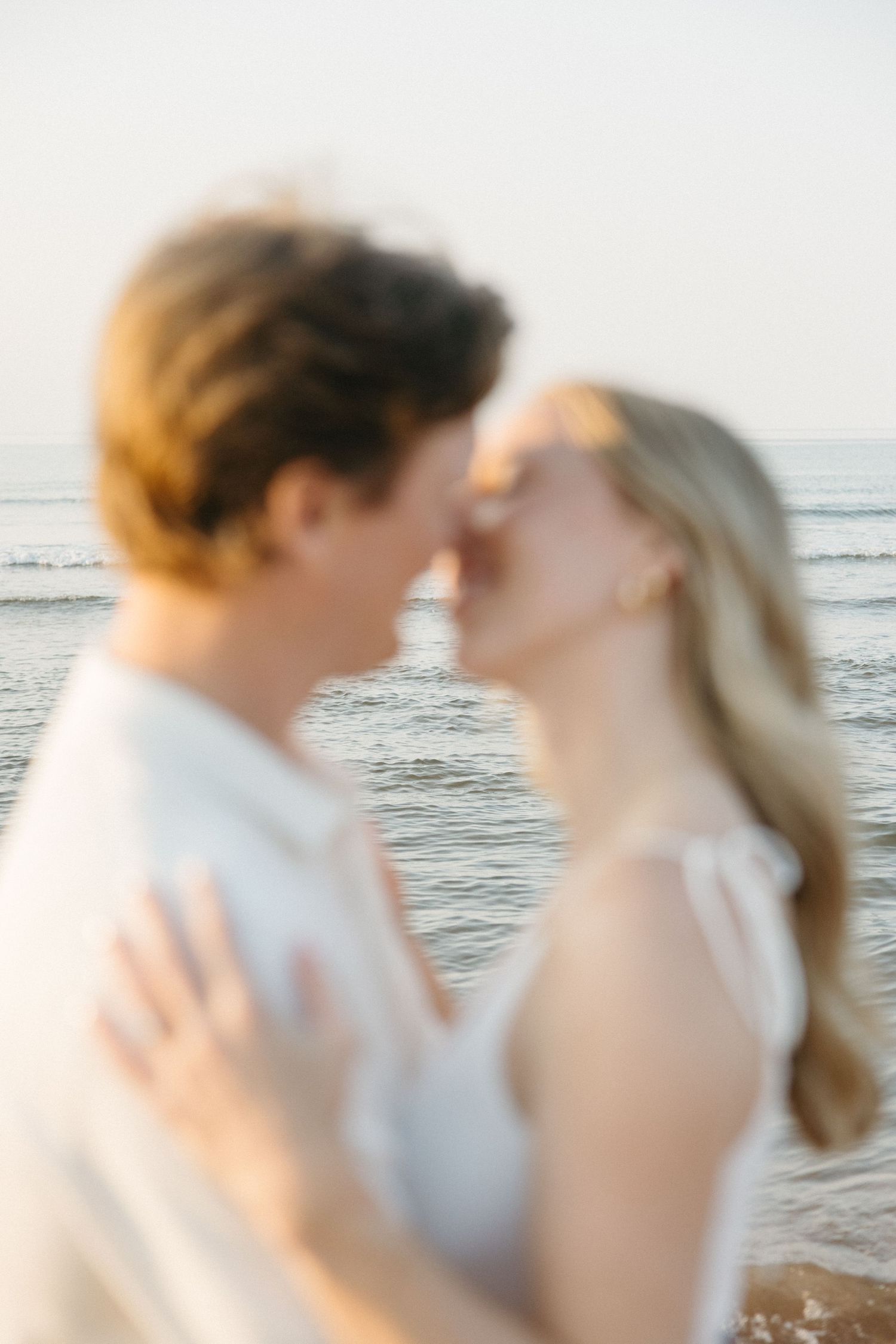 Blurred romantic couple almost kissing on a beach at sunset with ocean waves in the background.