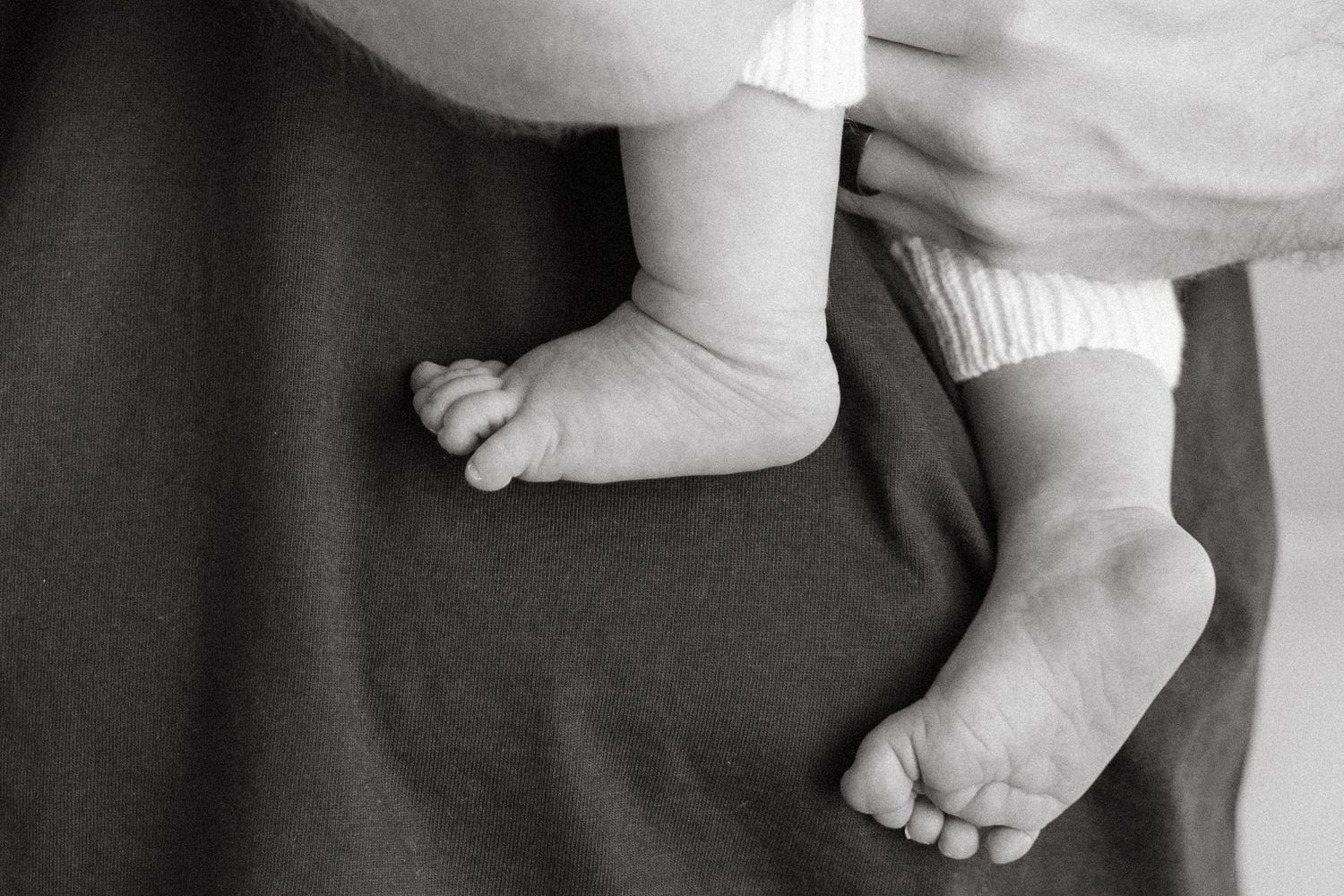 Black and white photo of tiny baby feet and hands against a light background.