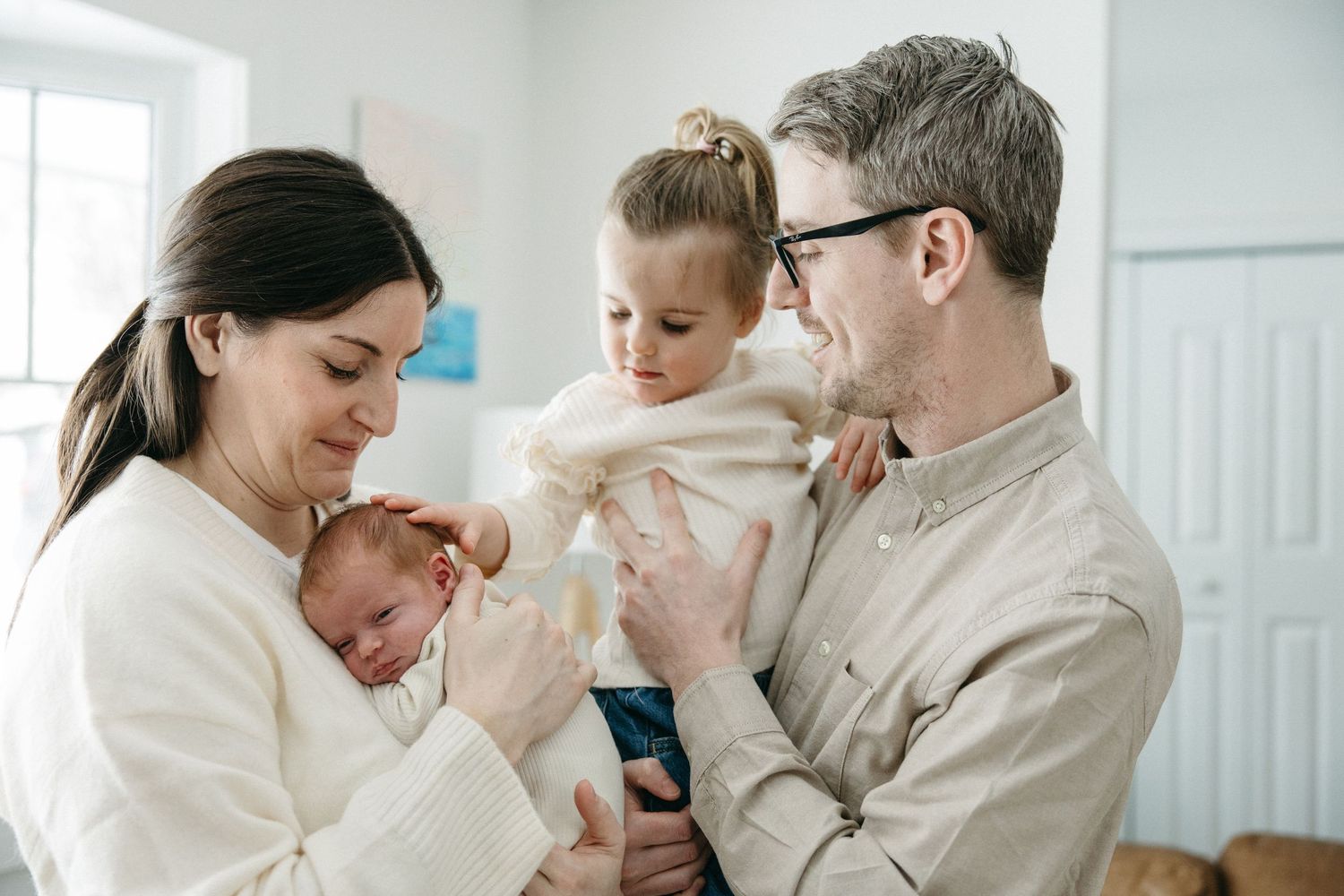 A family shares an intimate moment together while holding their newborn baby in a bright room.