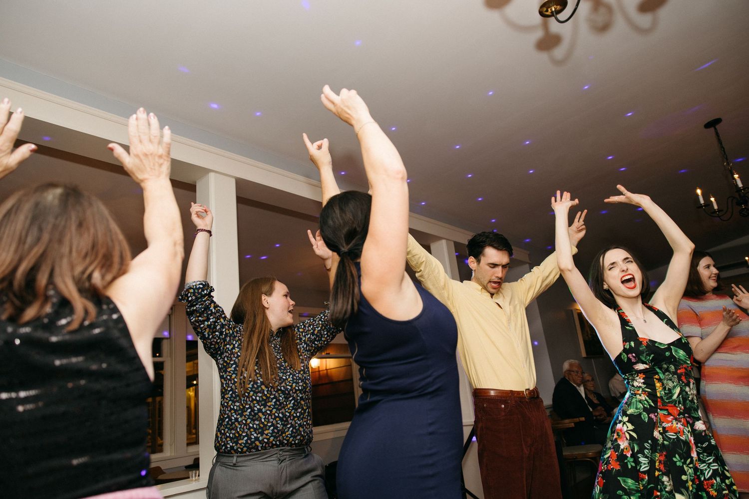 Wedding guests celebrate on dance floor with hands raised during lively reception party.