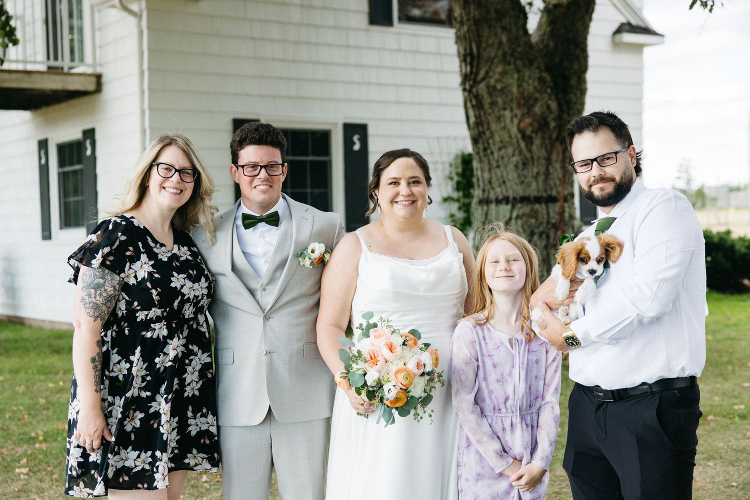 Family group portrait with bride holding bouquet, groom in bow tie, and guests holding a dog.
