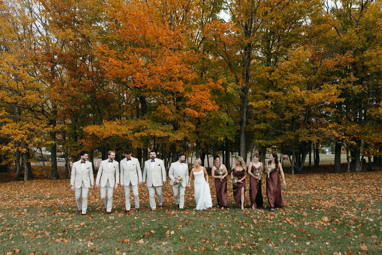Wedding party group photo with autumn foliage backdrop in orange and gold tones.