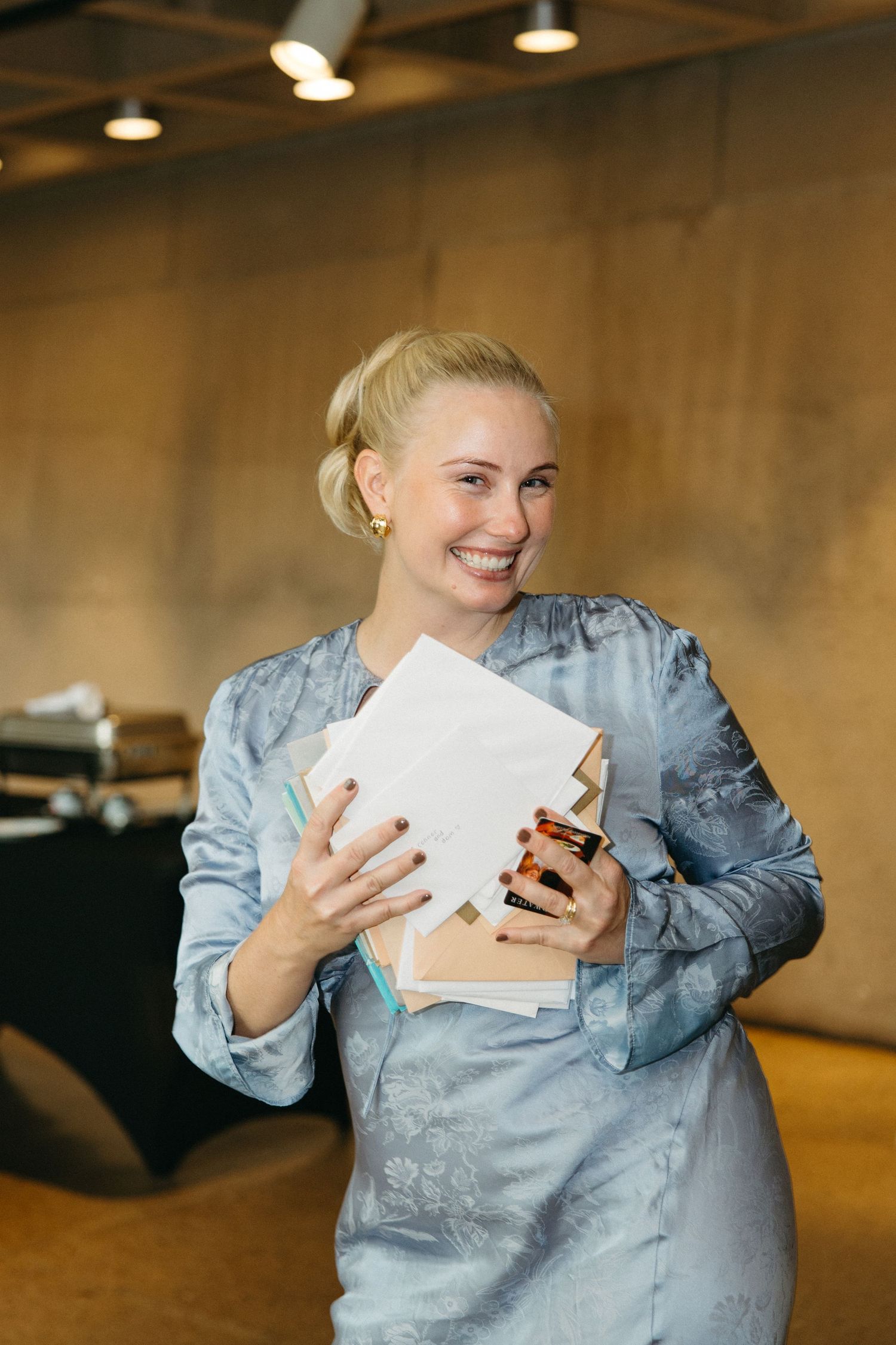 A person in a light blue denim jacket laughs while looking at their phone and holding papers.