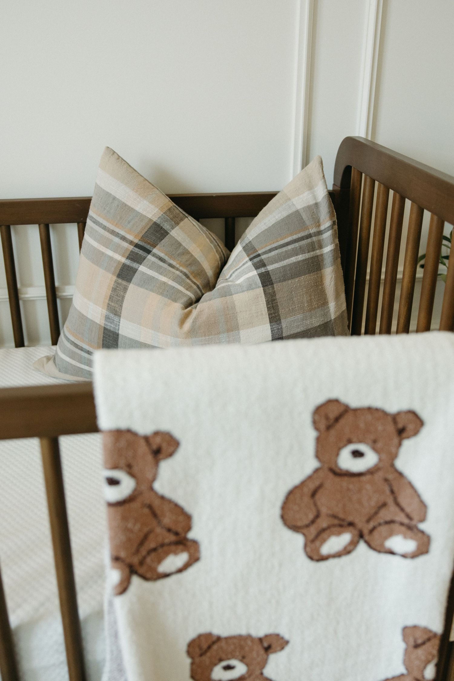 Decorative pillows with brown bear pattern on wooden chair in neutral nursery.