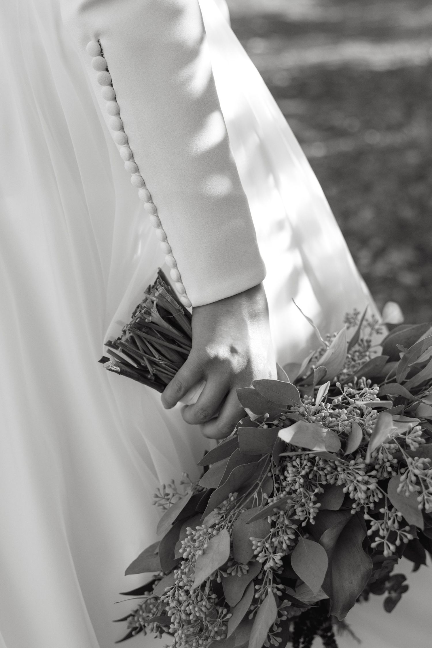 A wedding bouquet with dark greenery and flowers held against a white dress.