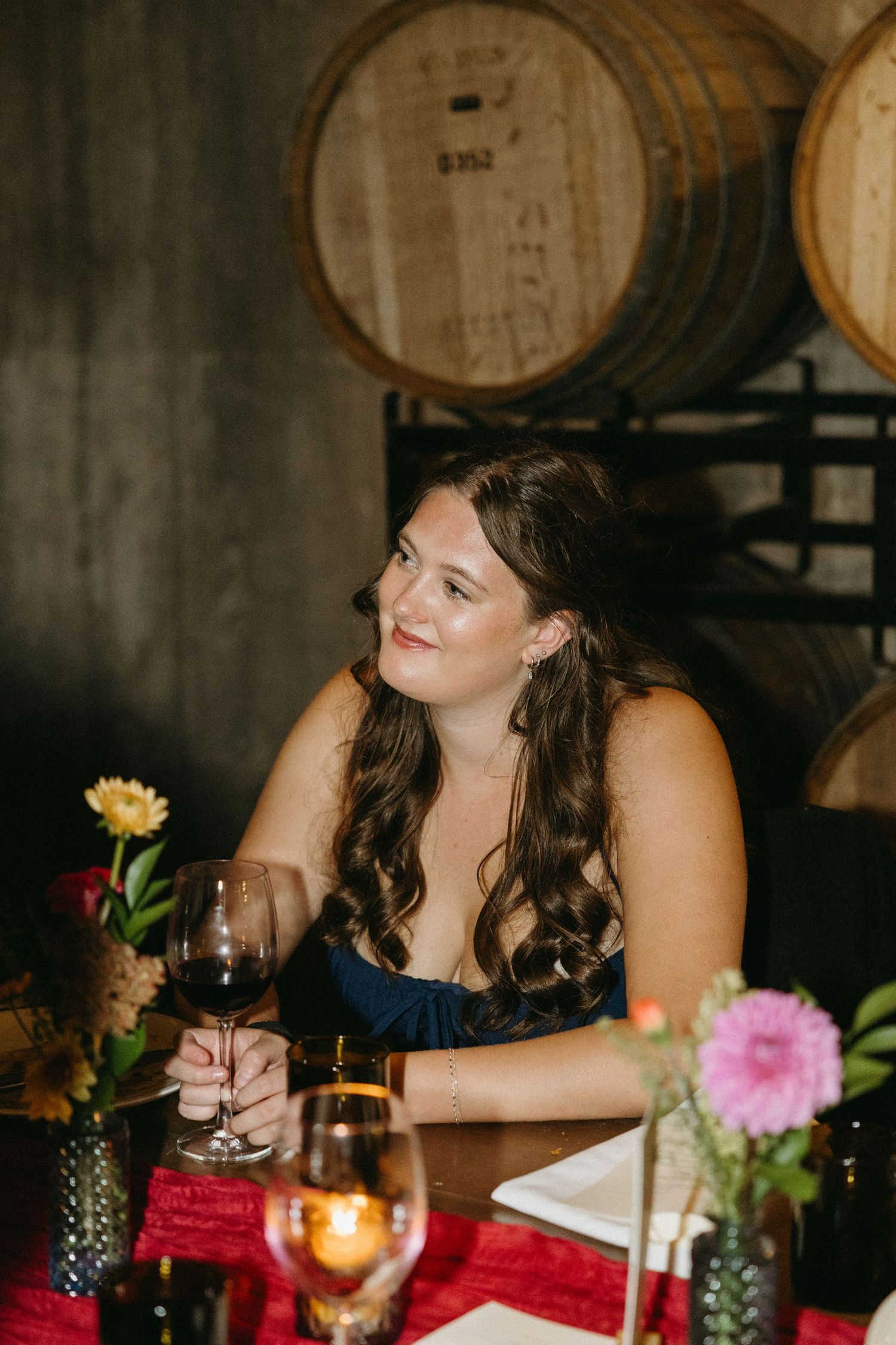 Guest in navy dress relaxing at decorated table with wine barrels and floral centerpieces.