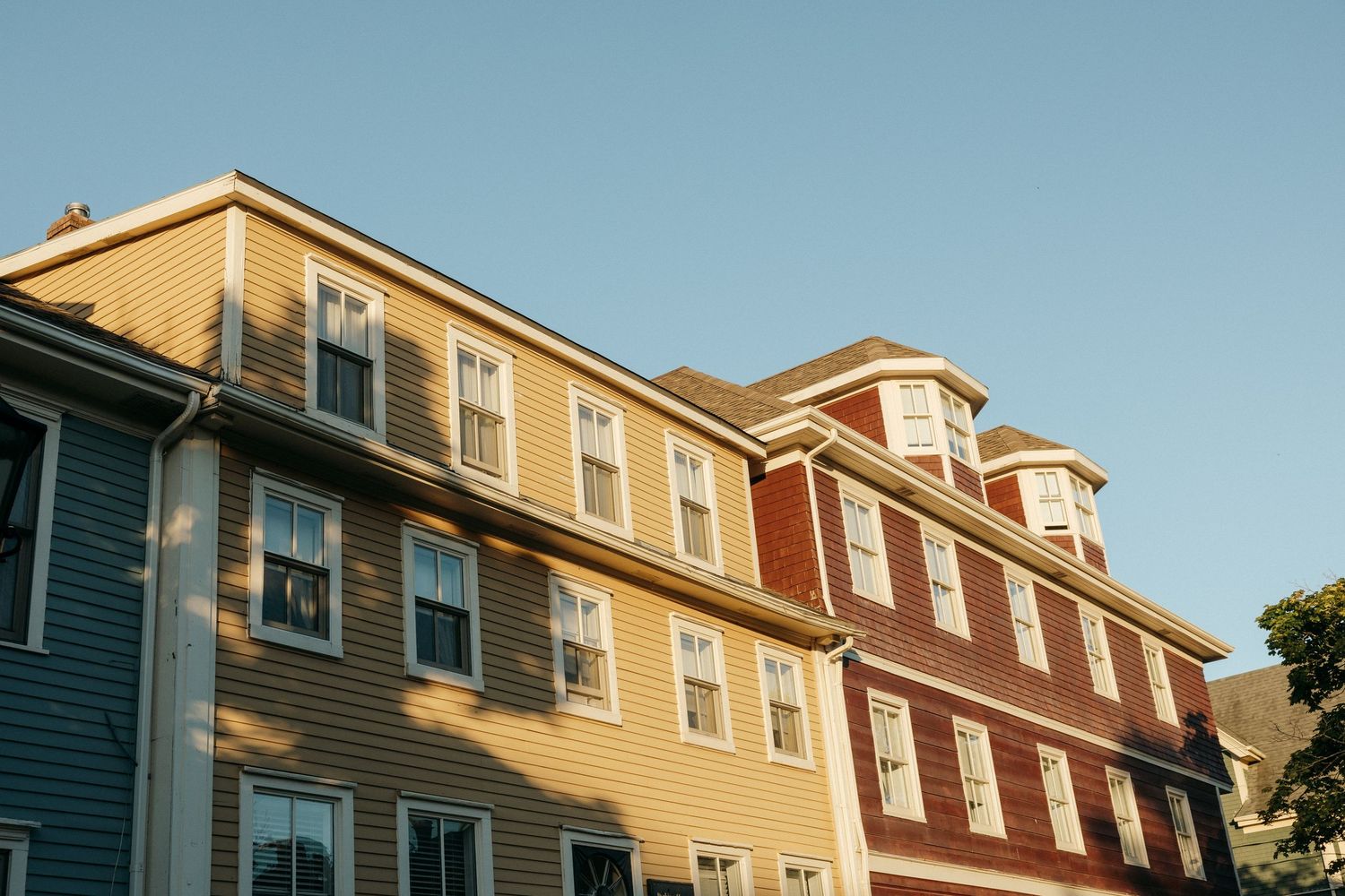 Row of traditional New England style houses with varied rooflines against blue sky.