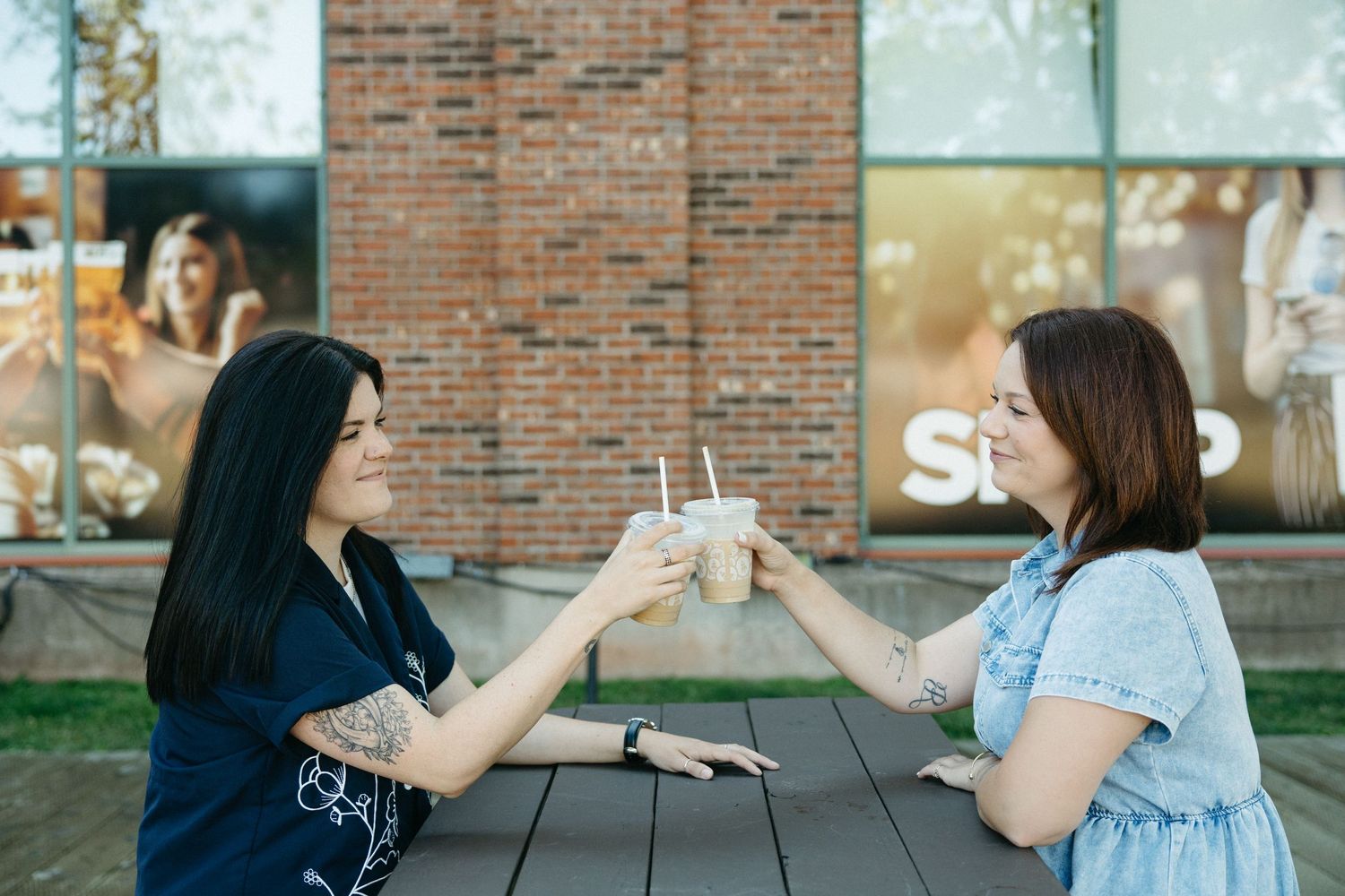 Friends toasting with iced drinks at an outdoor table near a storefront.