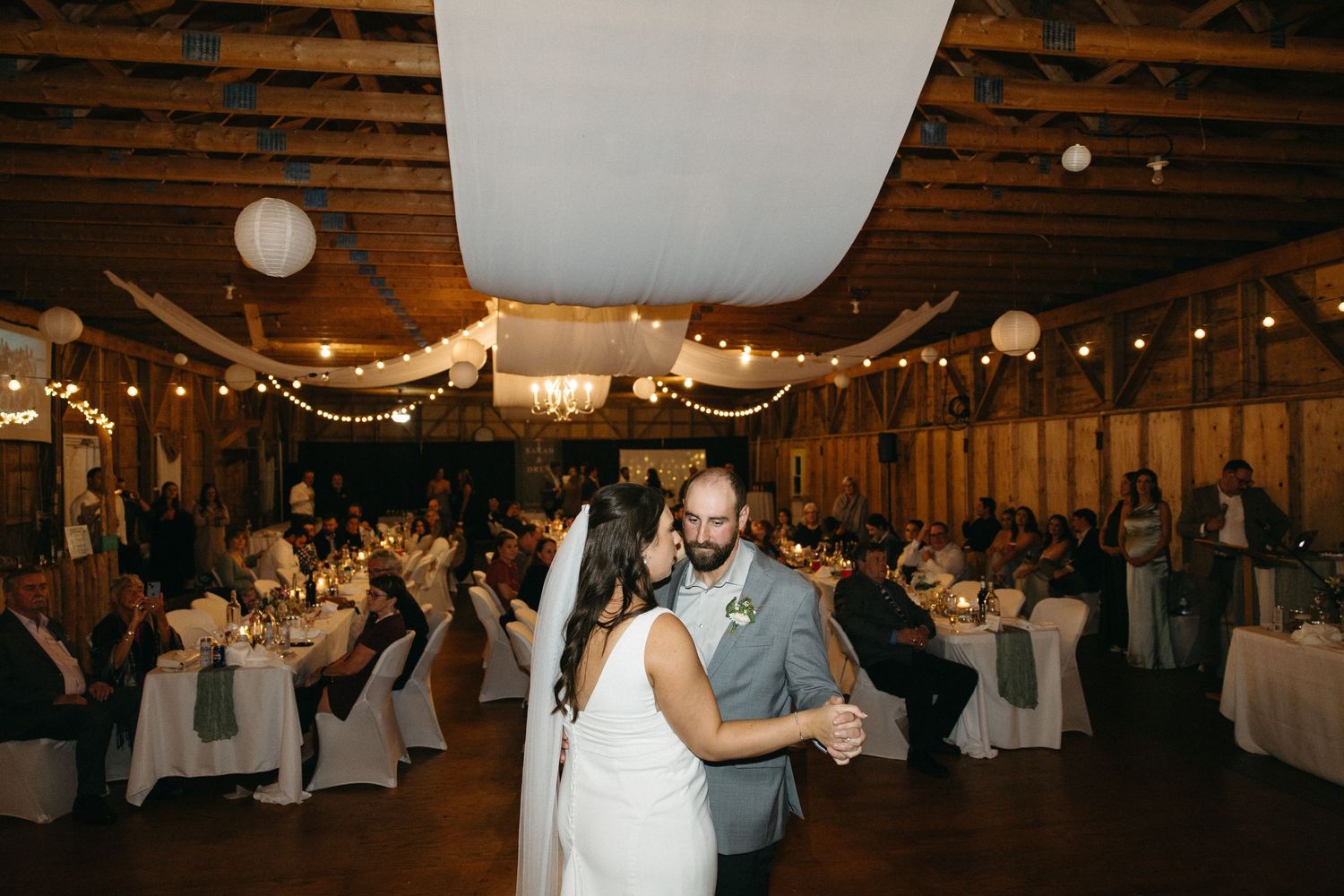 Rustic barn wedding reception venue decorated with string lights and white fabric draping.