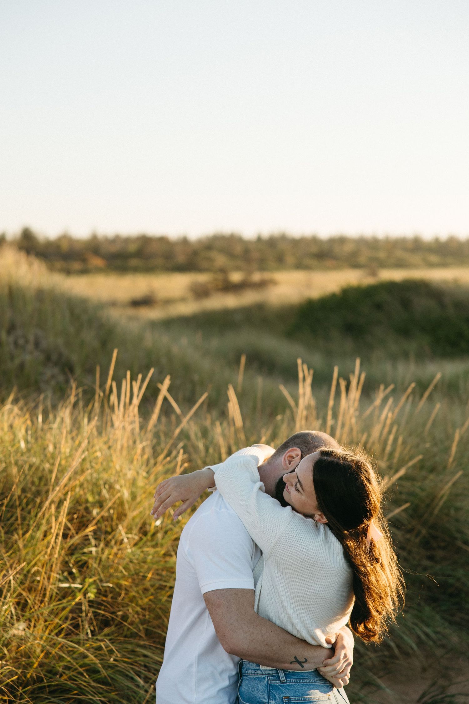 Romantic couple embracing in a field of tall grass during sunset.