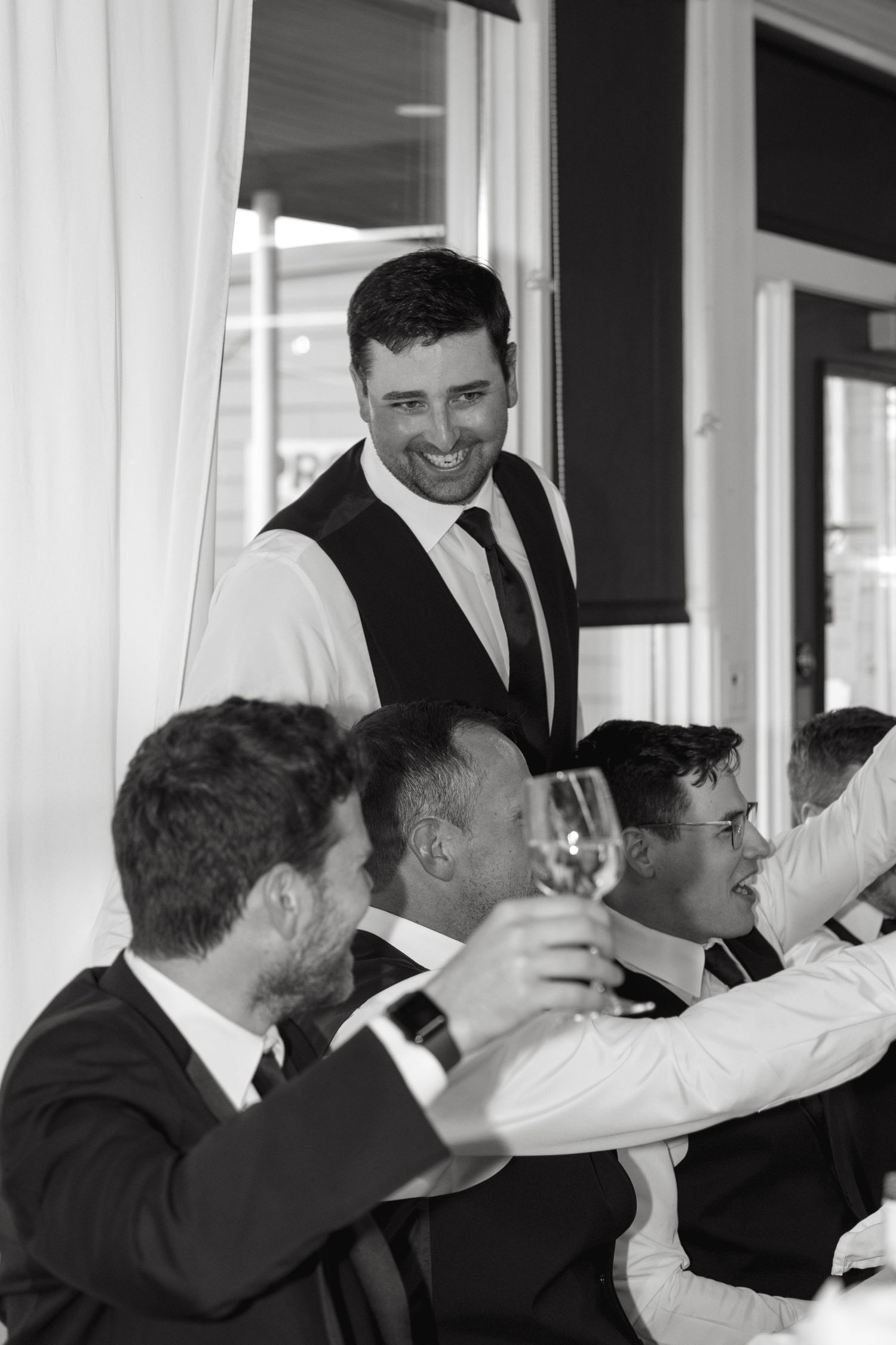 Groomsmen in formal attire raise their glasses in a celebratory toast at a wedding reception.