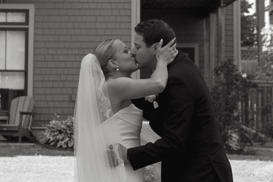 Romantic wedding couple sharing a kiss under a white veil at their outdoor ceremony.