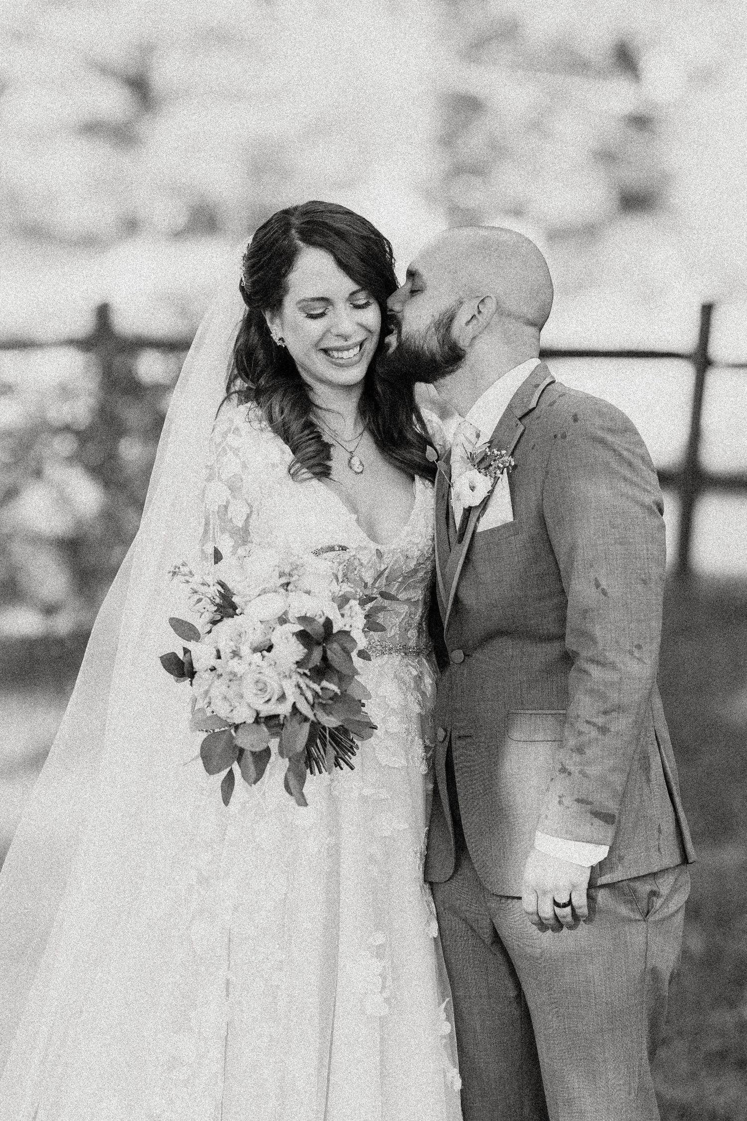 A joyful black and white wedding photo of a couple sharing an intimate moment with the bride holding a floral bouquet.