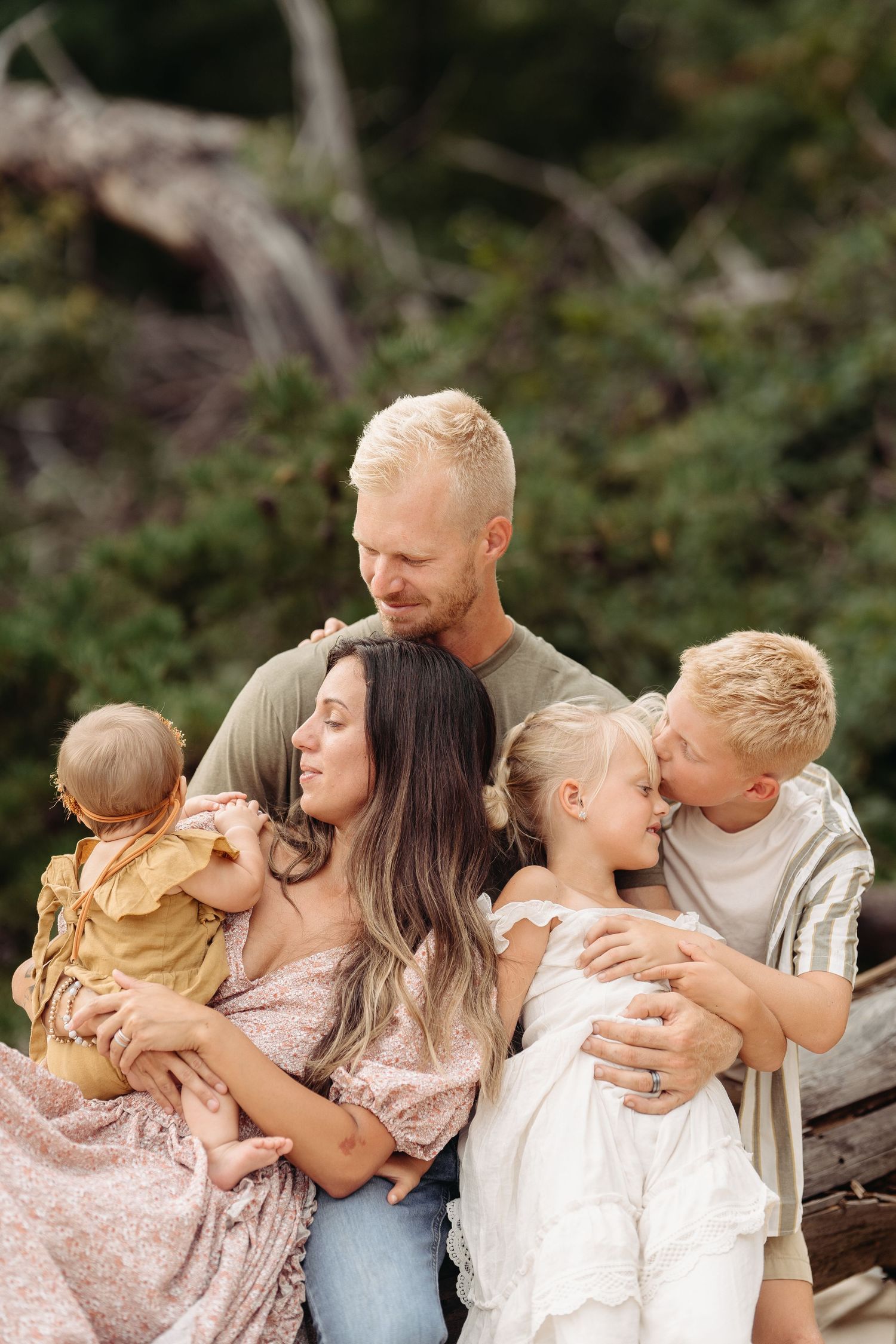 A family of five sits together outdoors sharing an intimate moment against a natural backdrop.
