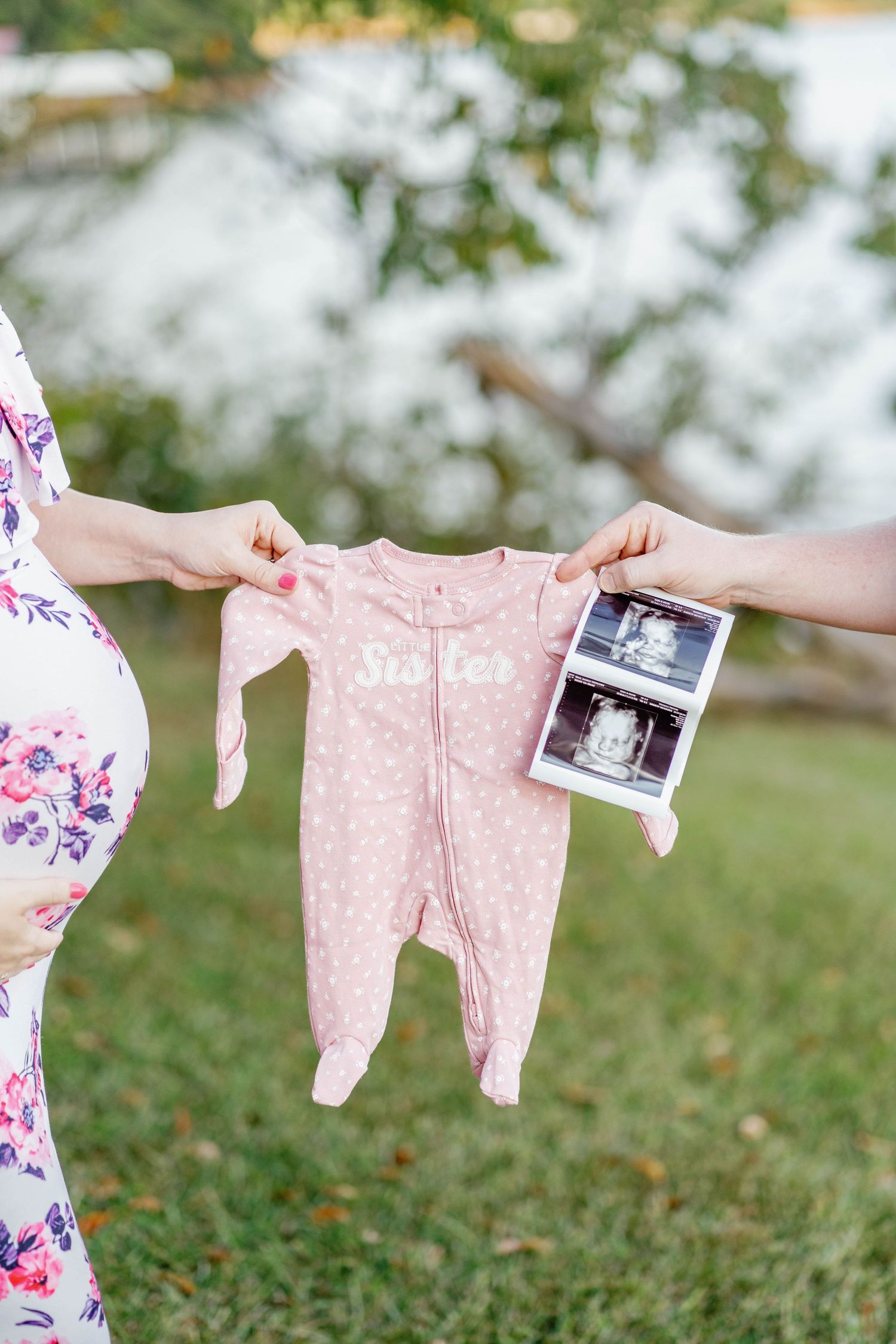 Pink polka dot baby sleeper and ultrasound photos displayed on a clothesline against a blurred green outdoor background.