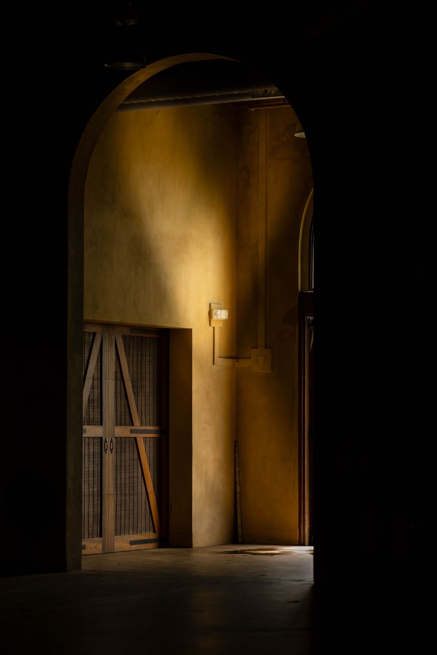 A dark hallway with arched doorways and dramatic shadows creates a moody architectural composition.