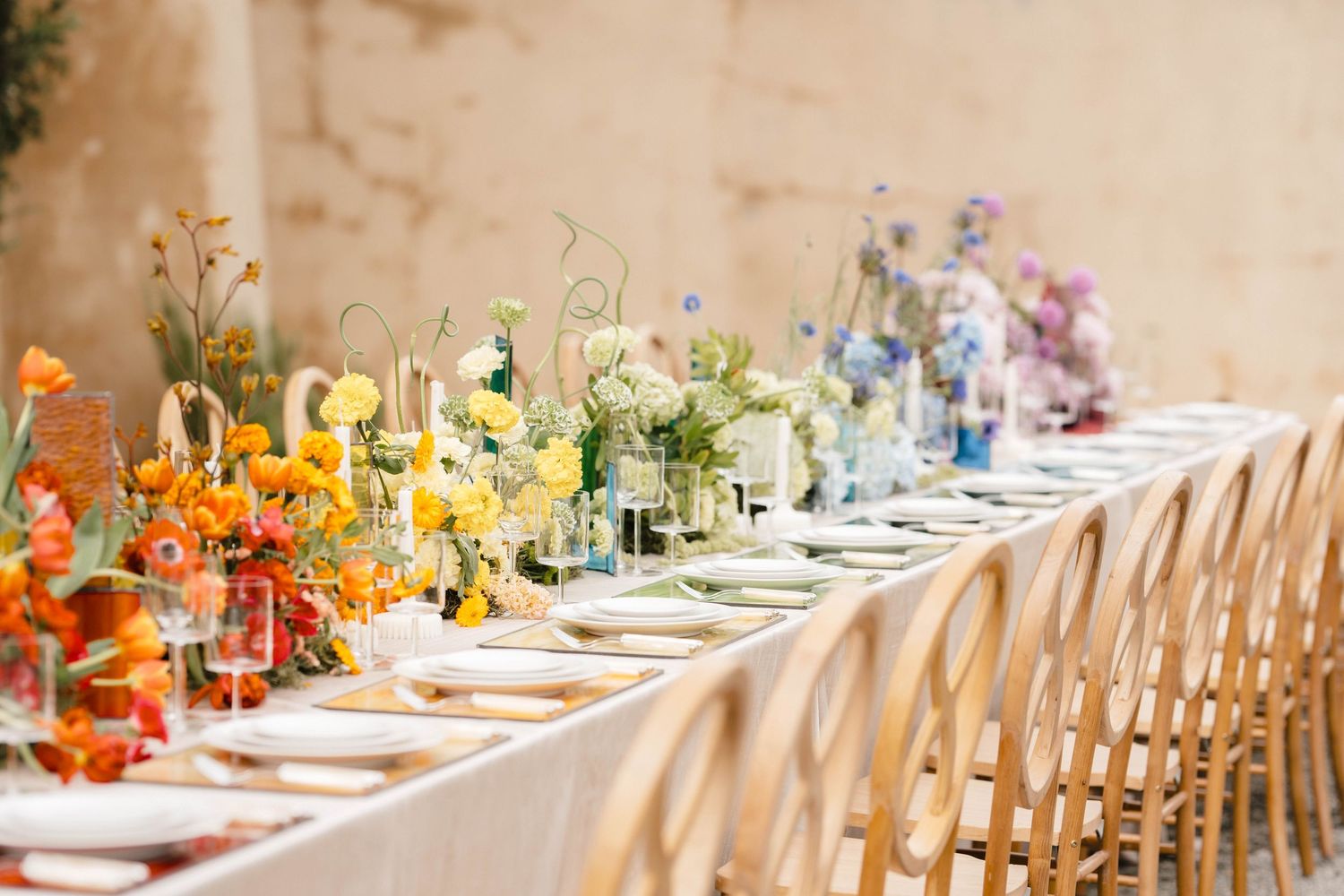 Long elegant dining table set with colorful floral centerpieces and place settings for a wedding reception.