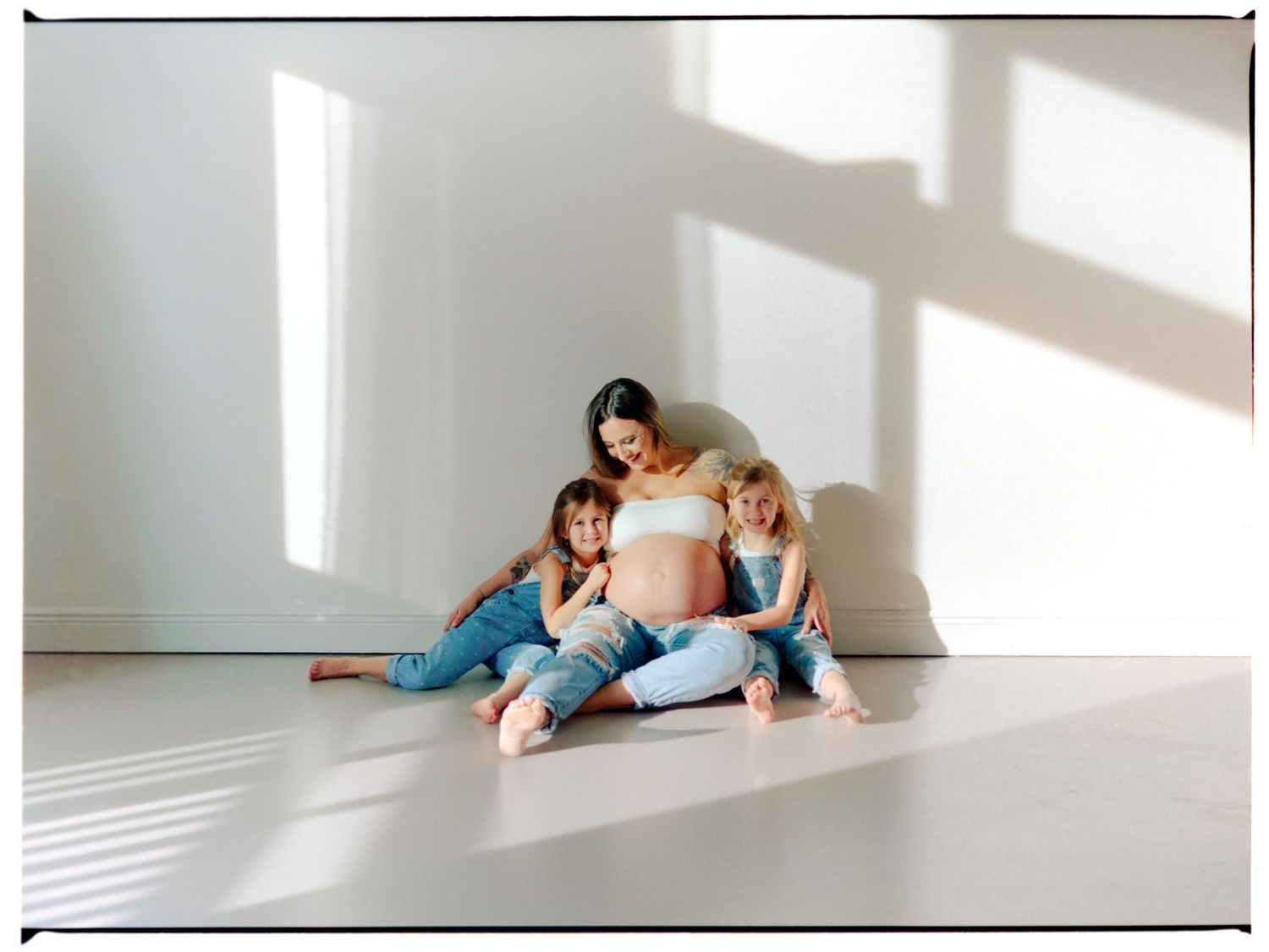 A family lies together on a white floor in a bright sunlit room with dramatic shadows casting across them.