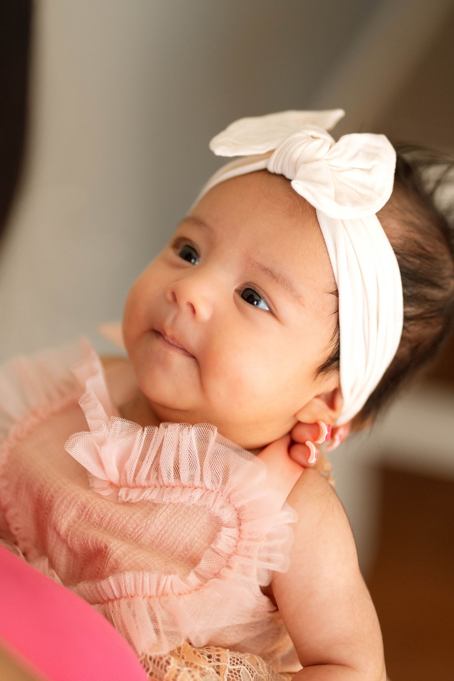 A baby wearing a pink ruffled dress and white bow headband gazes upward in a series of connected portrait shots.