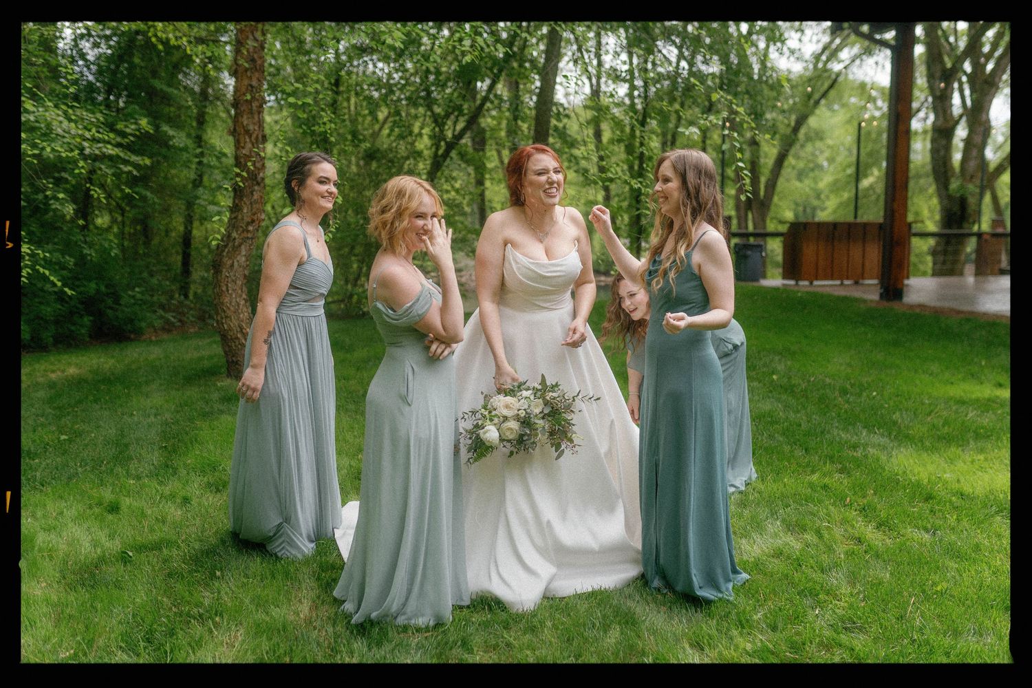 Bridesmaids in pale blue dresses pose together on a grassy lawn during an outdoor wedding celebration.
