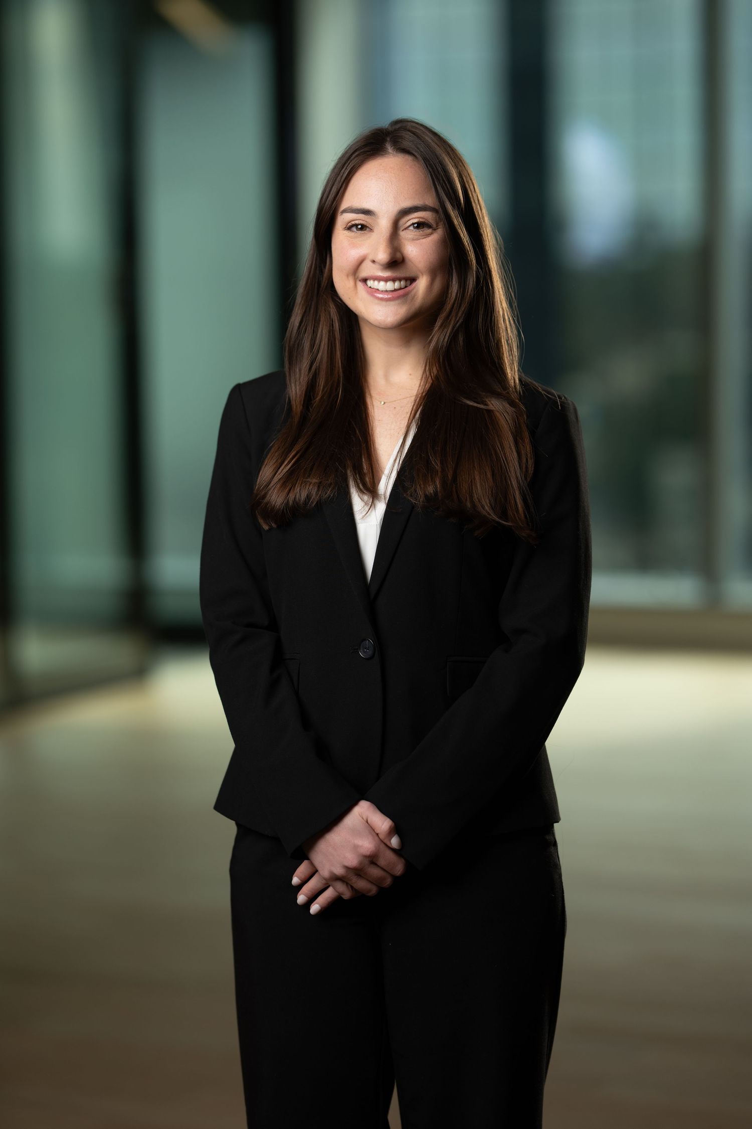 Young professional woman in black blazer smiling confidently in modern office corridor for corporate headshot.