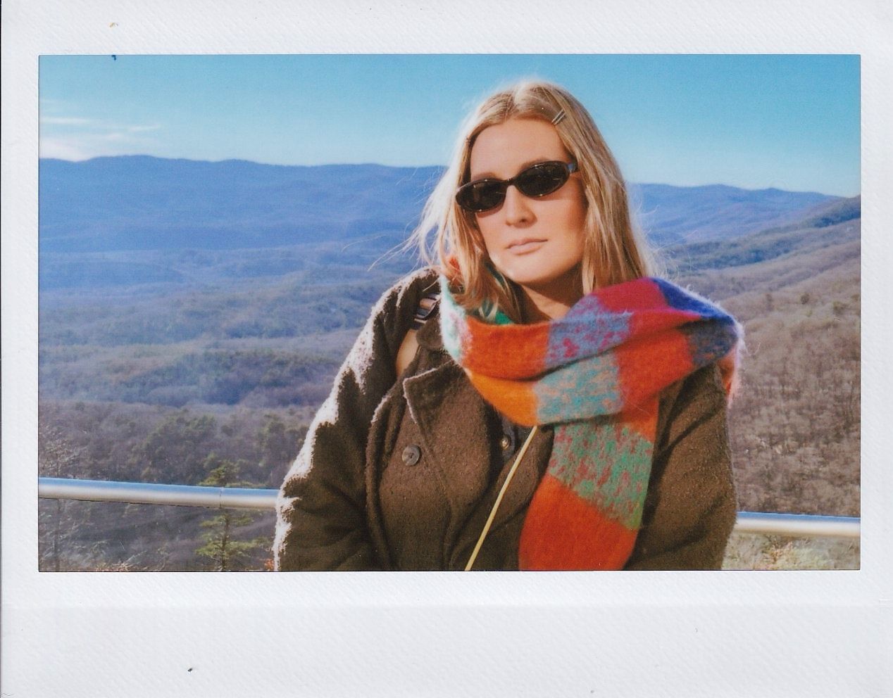 Person in brown jacket and colorful scarf enjoys scenic mountain views on a clear autumn day.