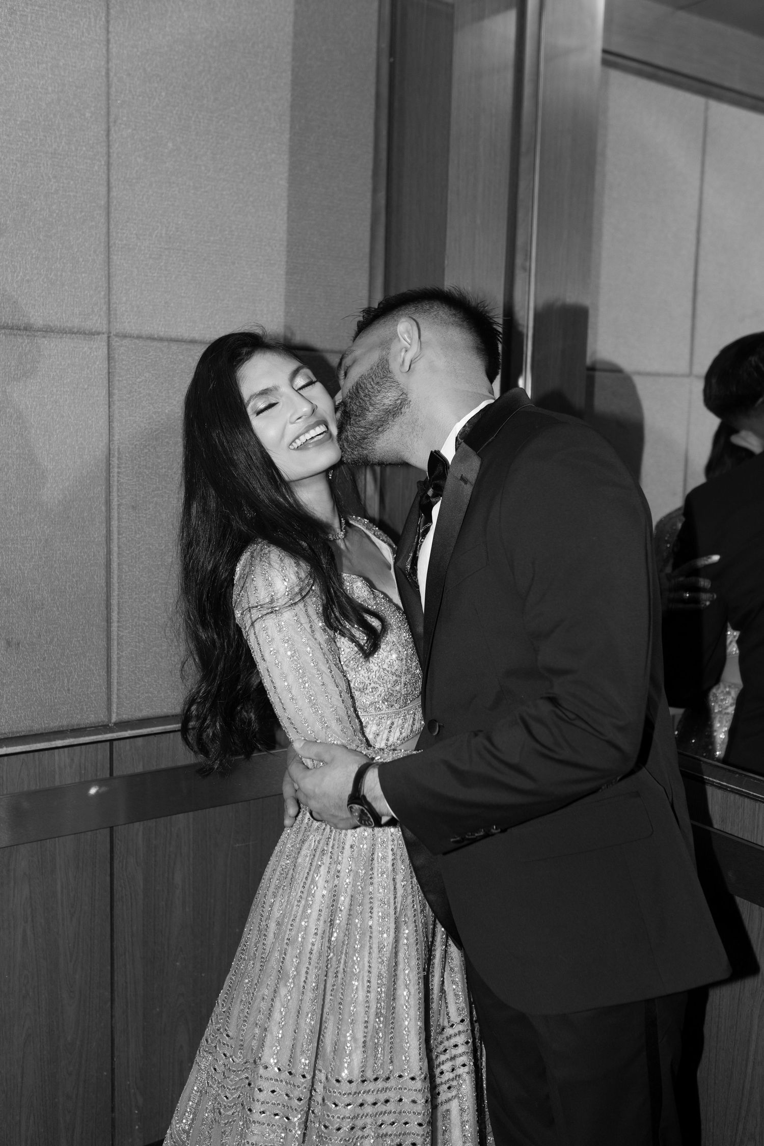 A couple in formal attire dance together, with the woman wearing a lace dress in a black and white photograph.