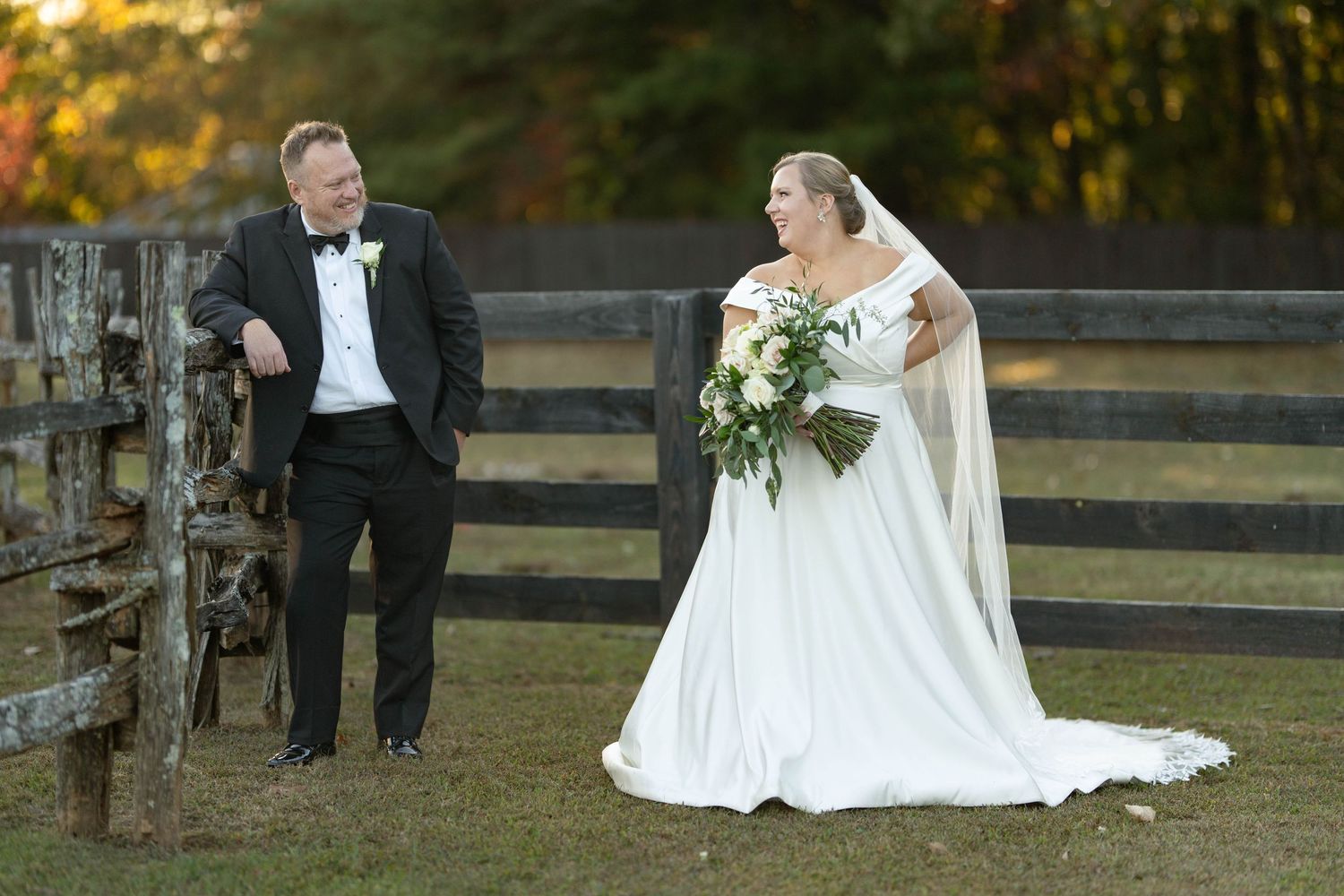 A bride and groom share intimate moments during their outdoor fall wedding photoshoot by a rustic wooden fence.