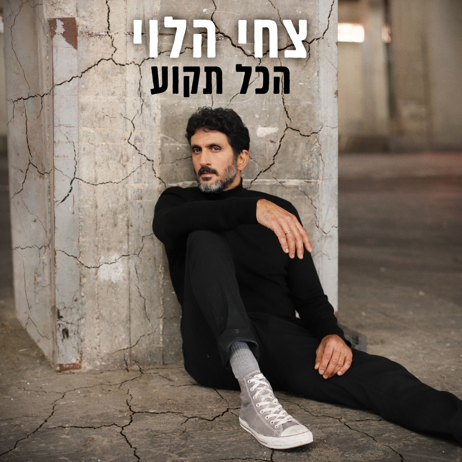 Album cover showing someone in all black clothing sitting against a concrete wall wearing white sneakers.