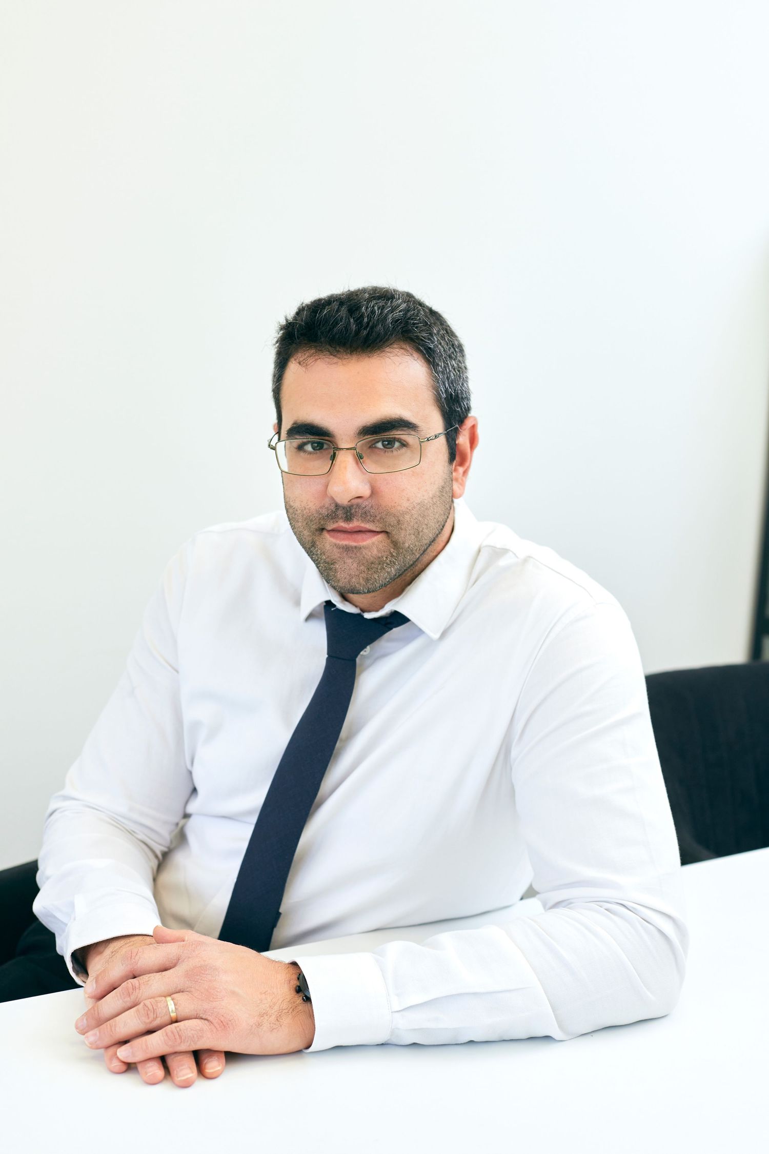 Professional man in business attire sits at desk in office setting.