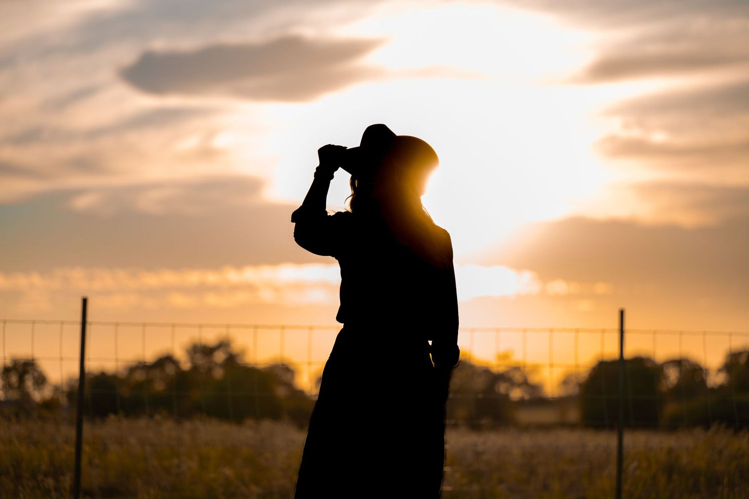 Silhouettes of cowboys against dramatic sunset sky.