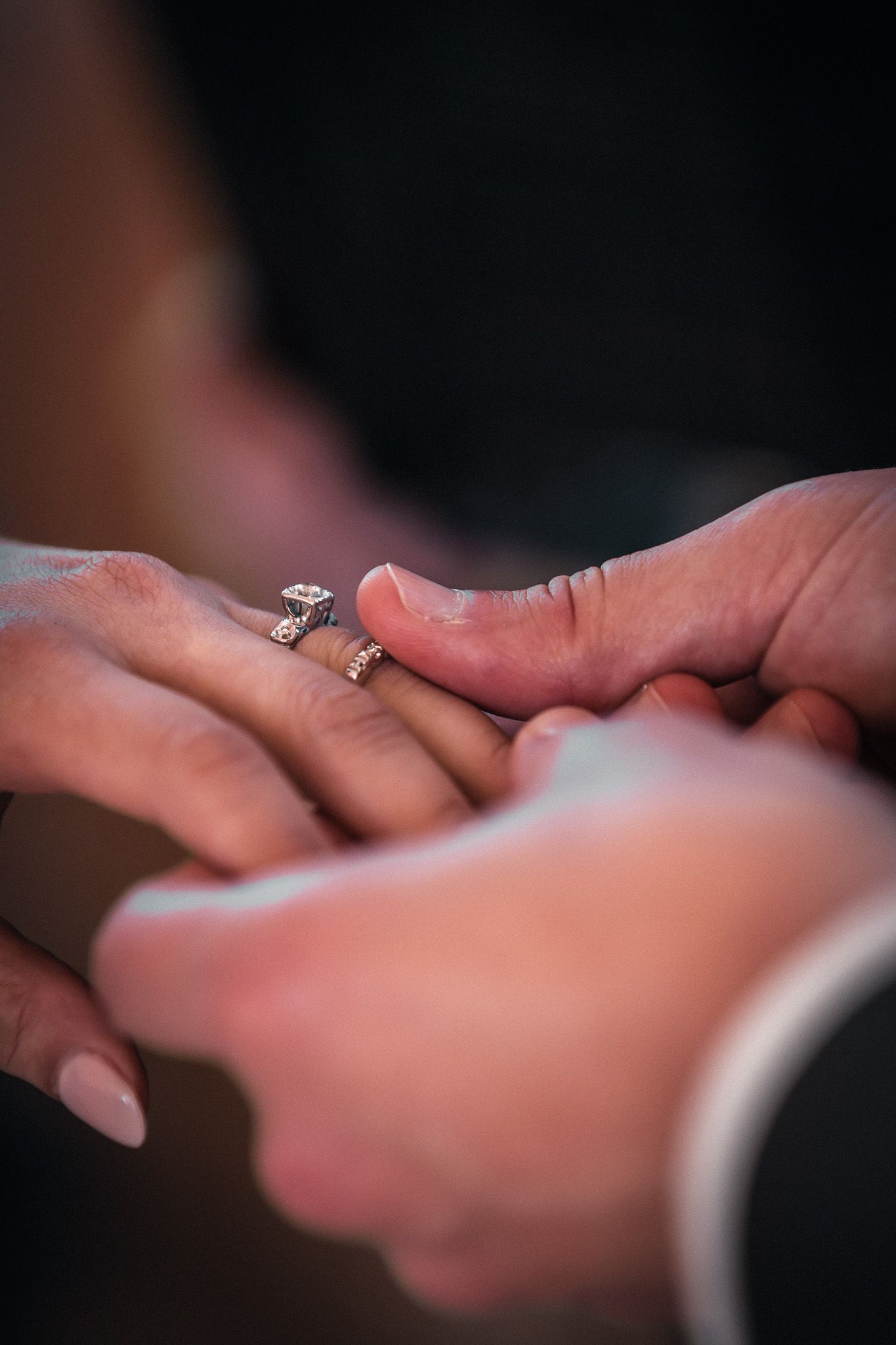 Close-up of two hands touching, woman wearing diamond engagement and wedding rings, romantic couple moment.
