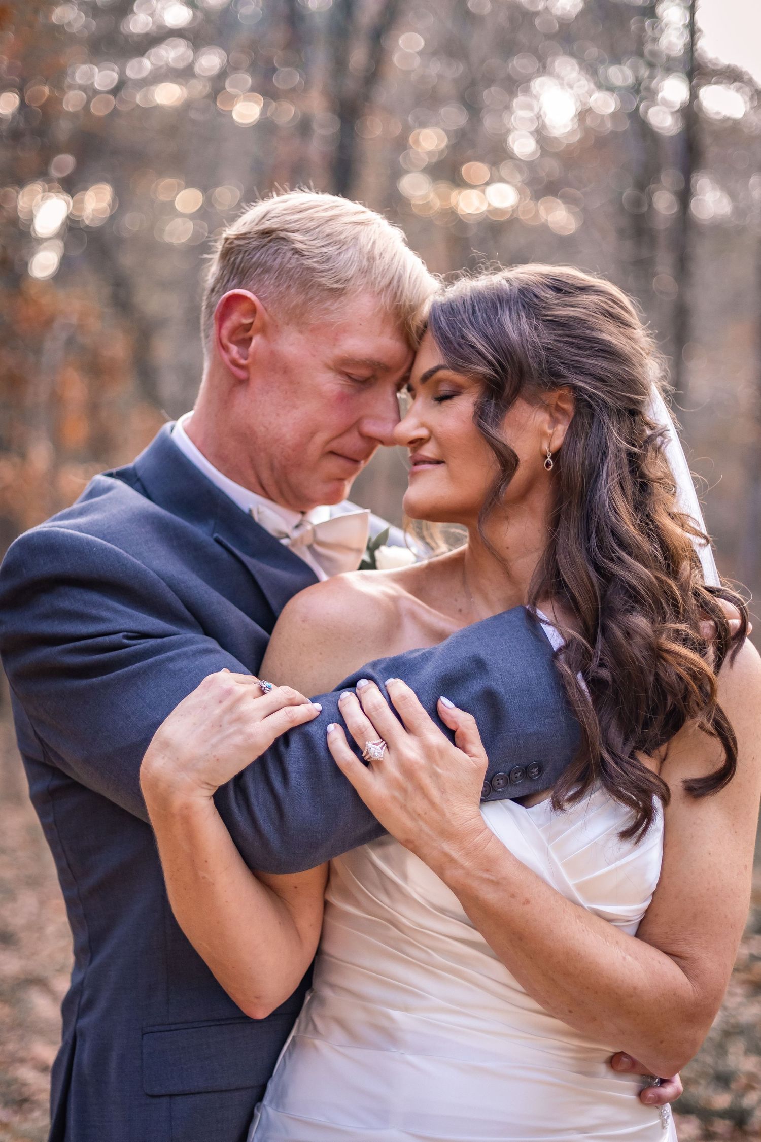 A romantic couple embraces intimately in an autumn forest setting wearing formal wedding attire.