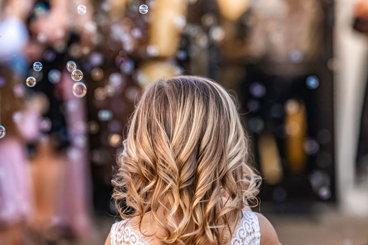 Blonde wavy hair styled in loose curls with bubbles floating in a festive party atmosphere.