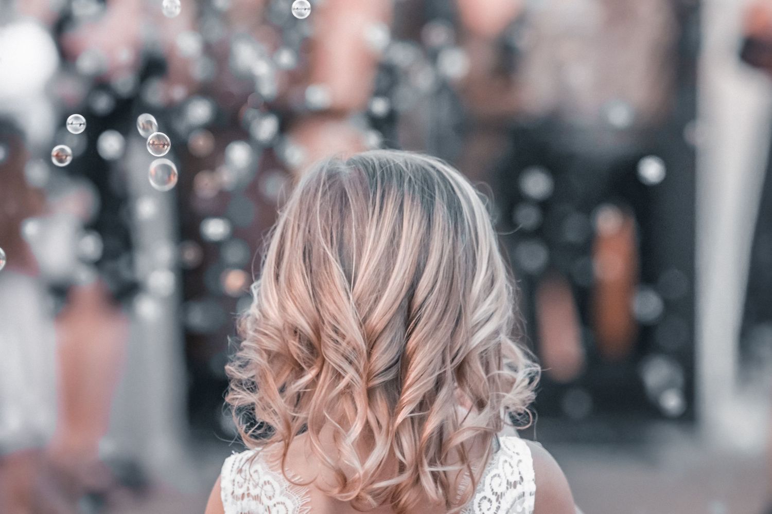 Bride with blonde ombre curls wearing a lace wedding dress poses in front of a bokeh light background.