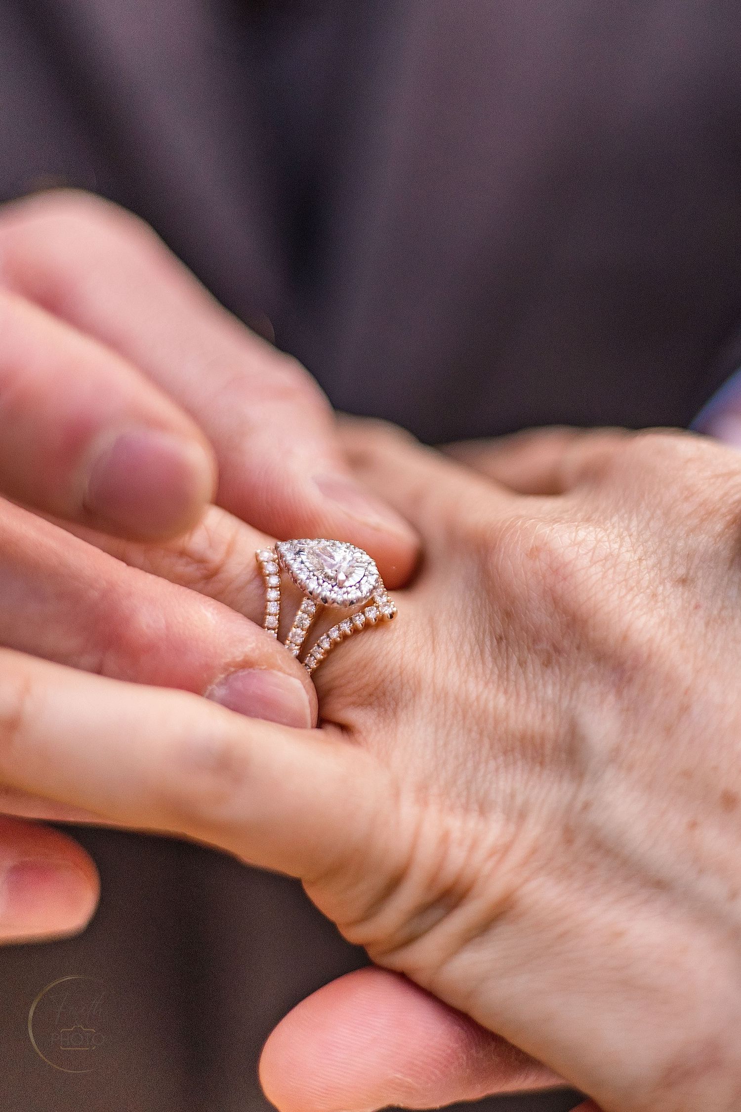 Close-up of a rose gold pear-shaped diamond halo engagement ring with wedding band stacked on a finger.
