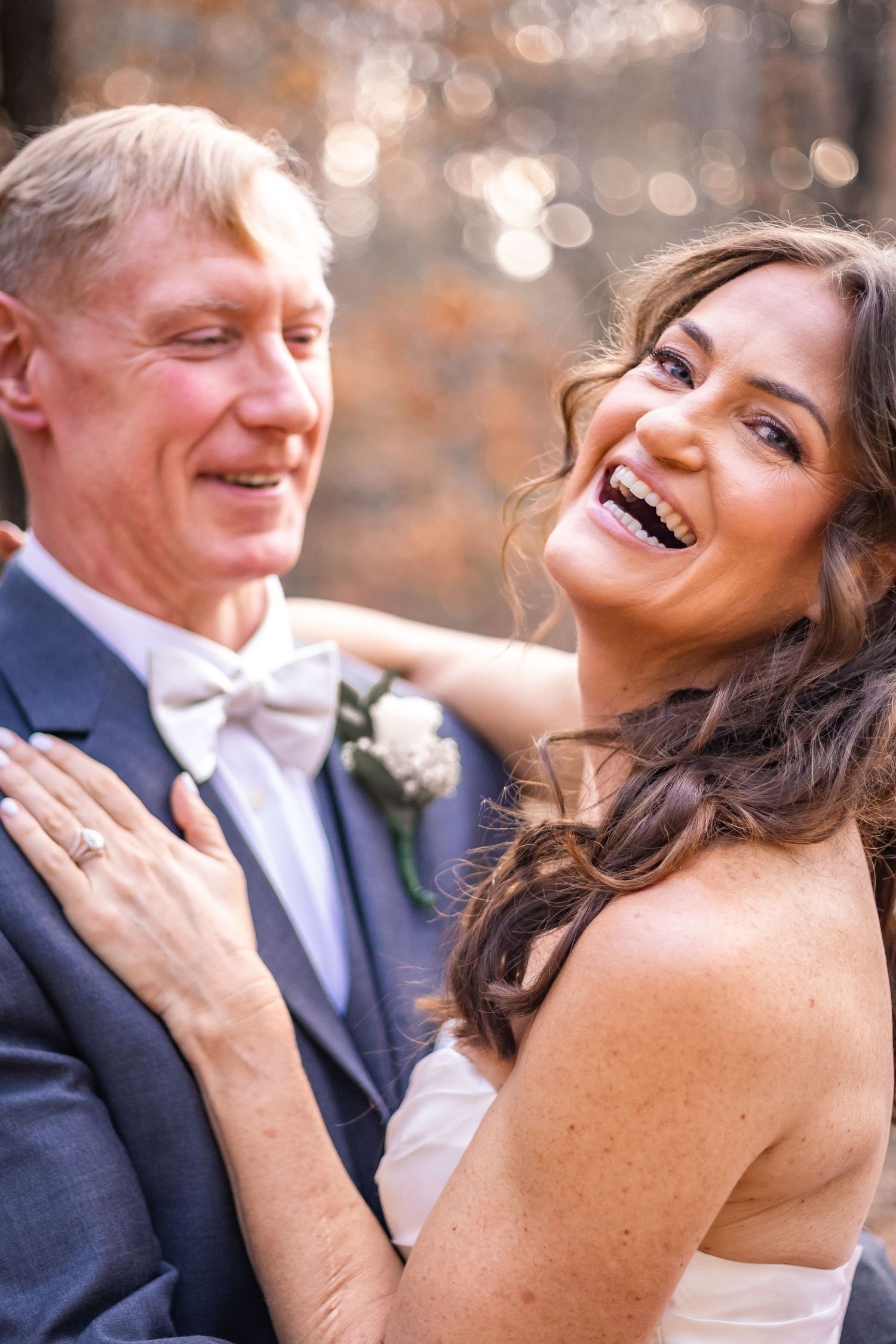 A happy couple shares joyful laughter during their outdoor wedding celebration with sparkling bokeh lights in background.