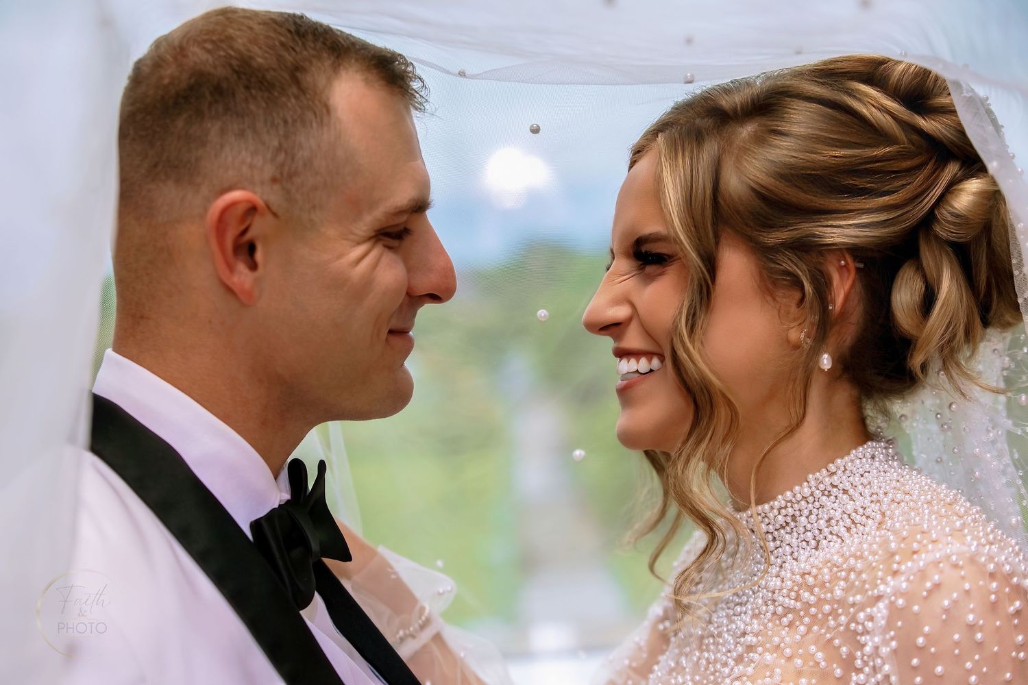 A bride and groom share a romantic moment, smiling at each other during their outdoor wedding ceremony.