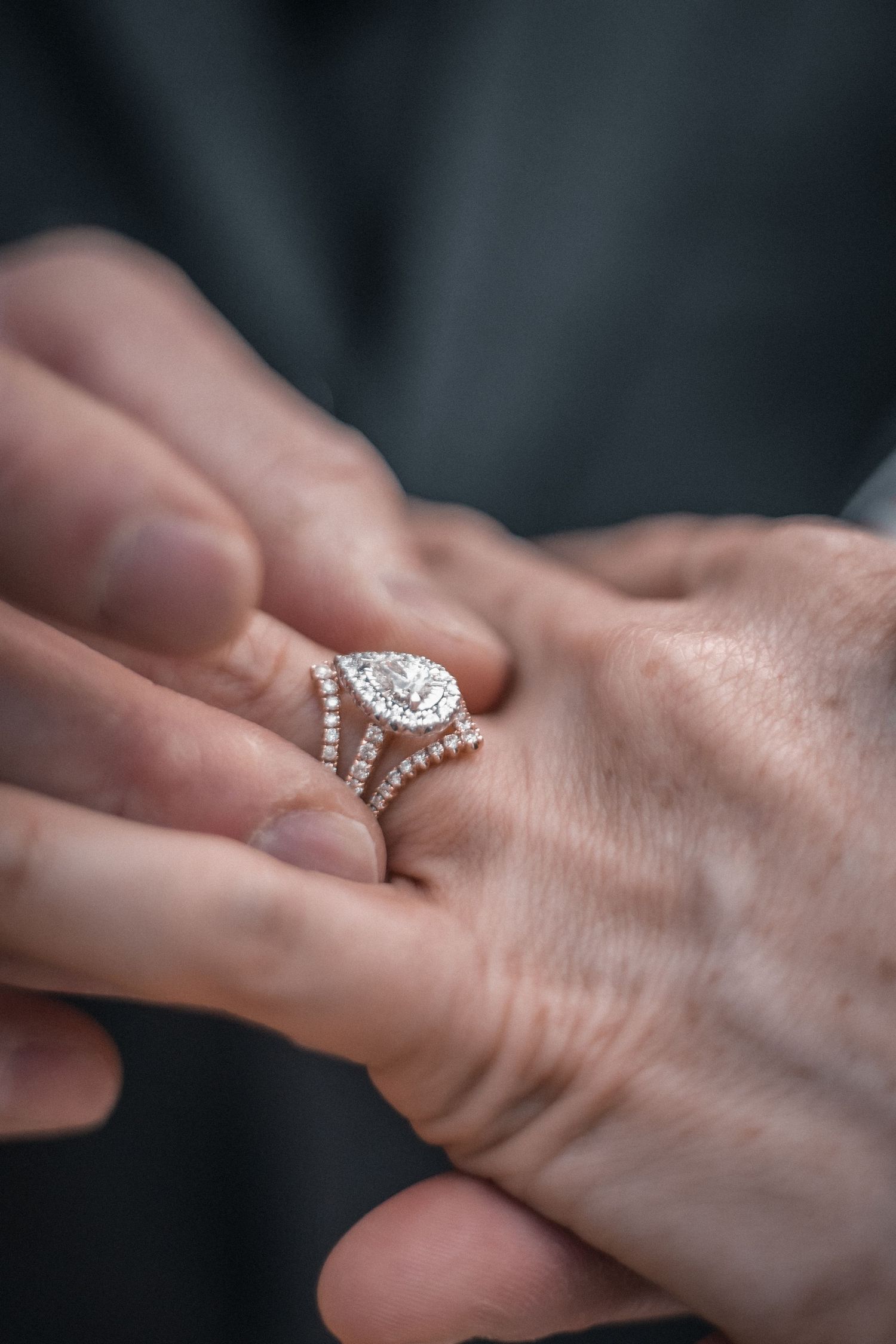 Close-up sequence showing a sparkling diamond engagement ring being placed on a woman's finger against dark background.