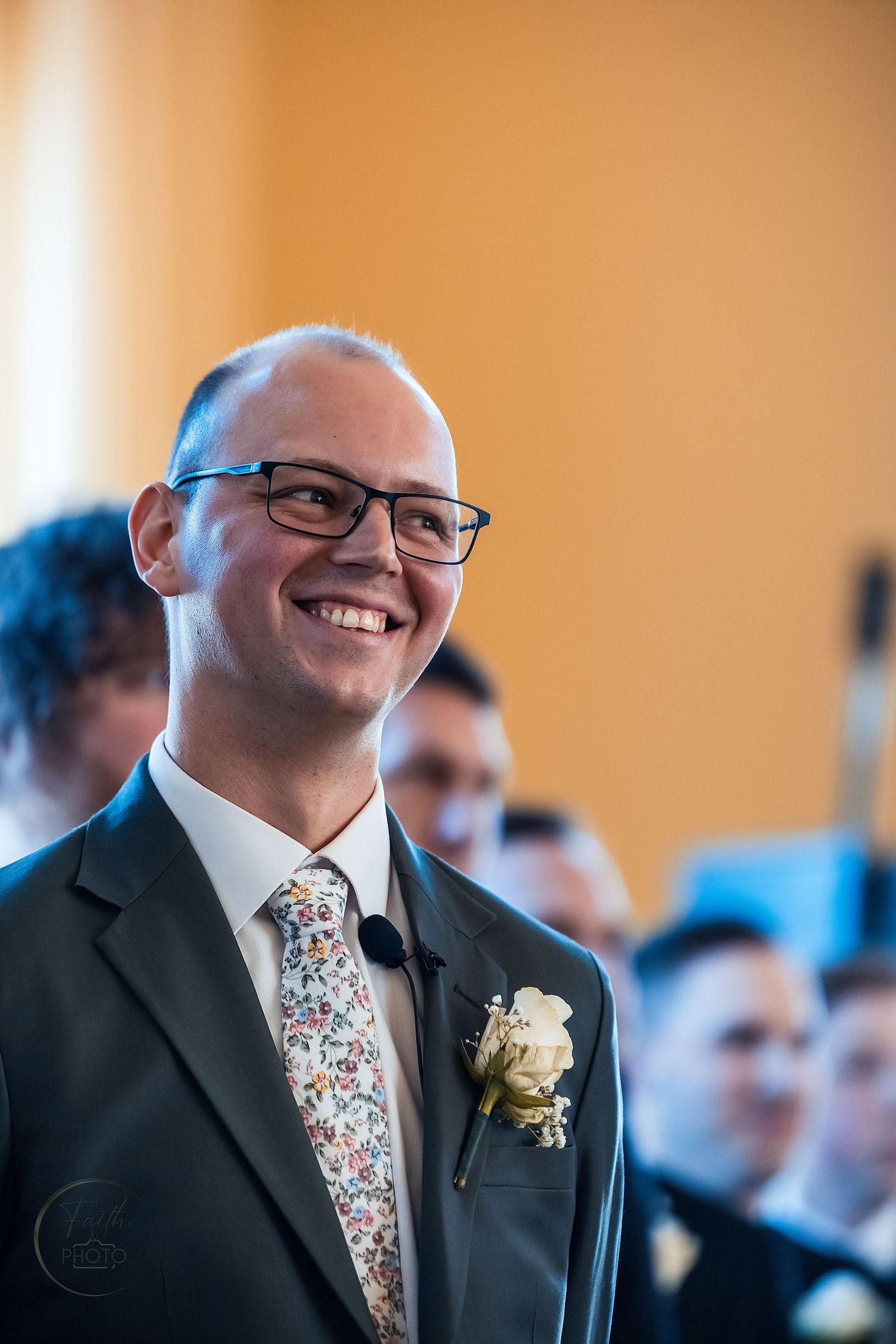 Smiling groom in gray suit with floral tie and boutonniere at wedding ceremony.