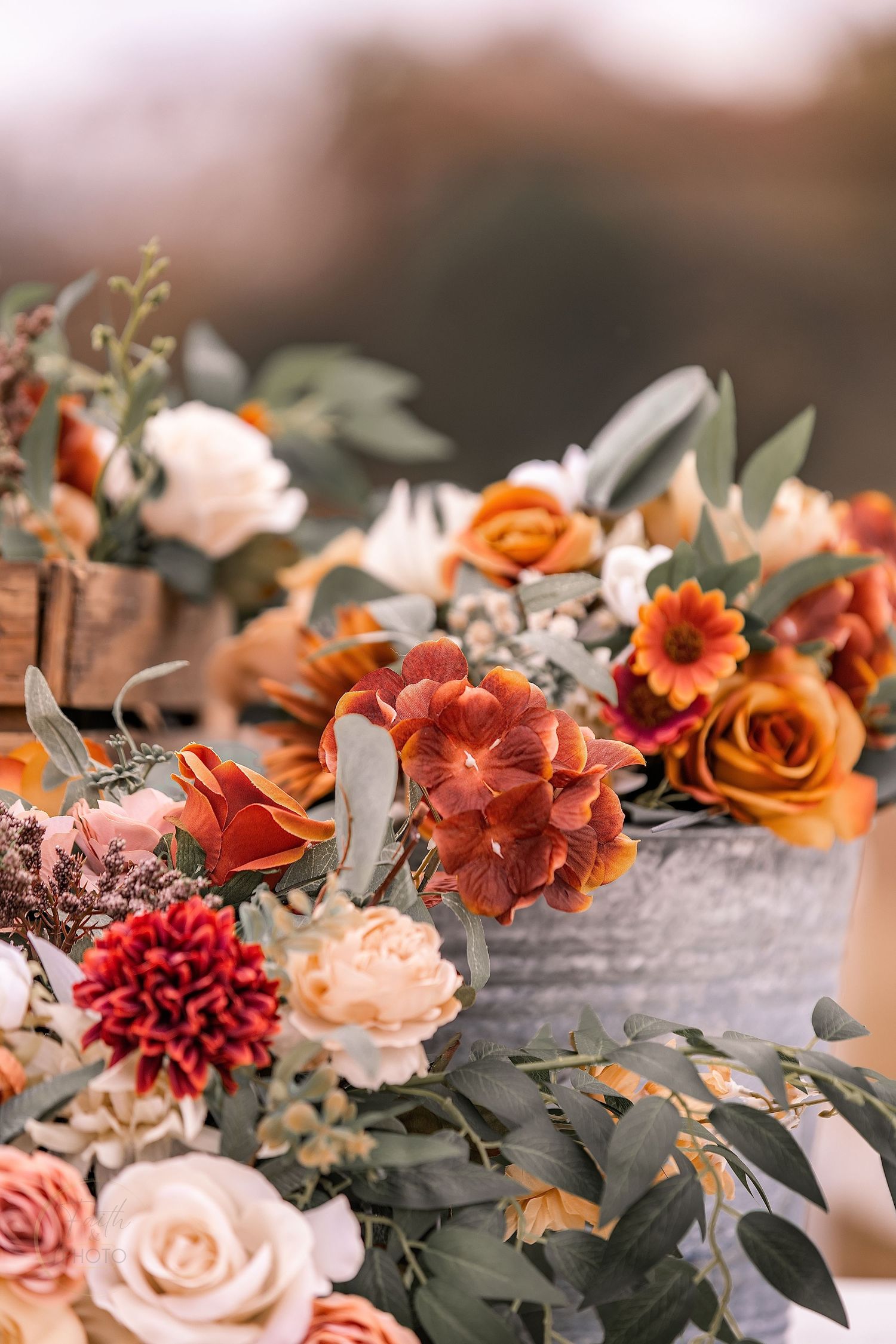 Rustic fall floral arrangements in metal and wooden containers featuring orange roses, red dahlias, and eucalyptus greenery.