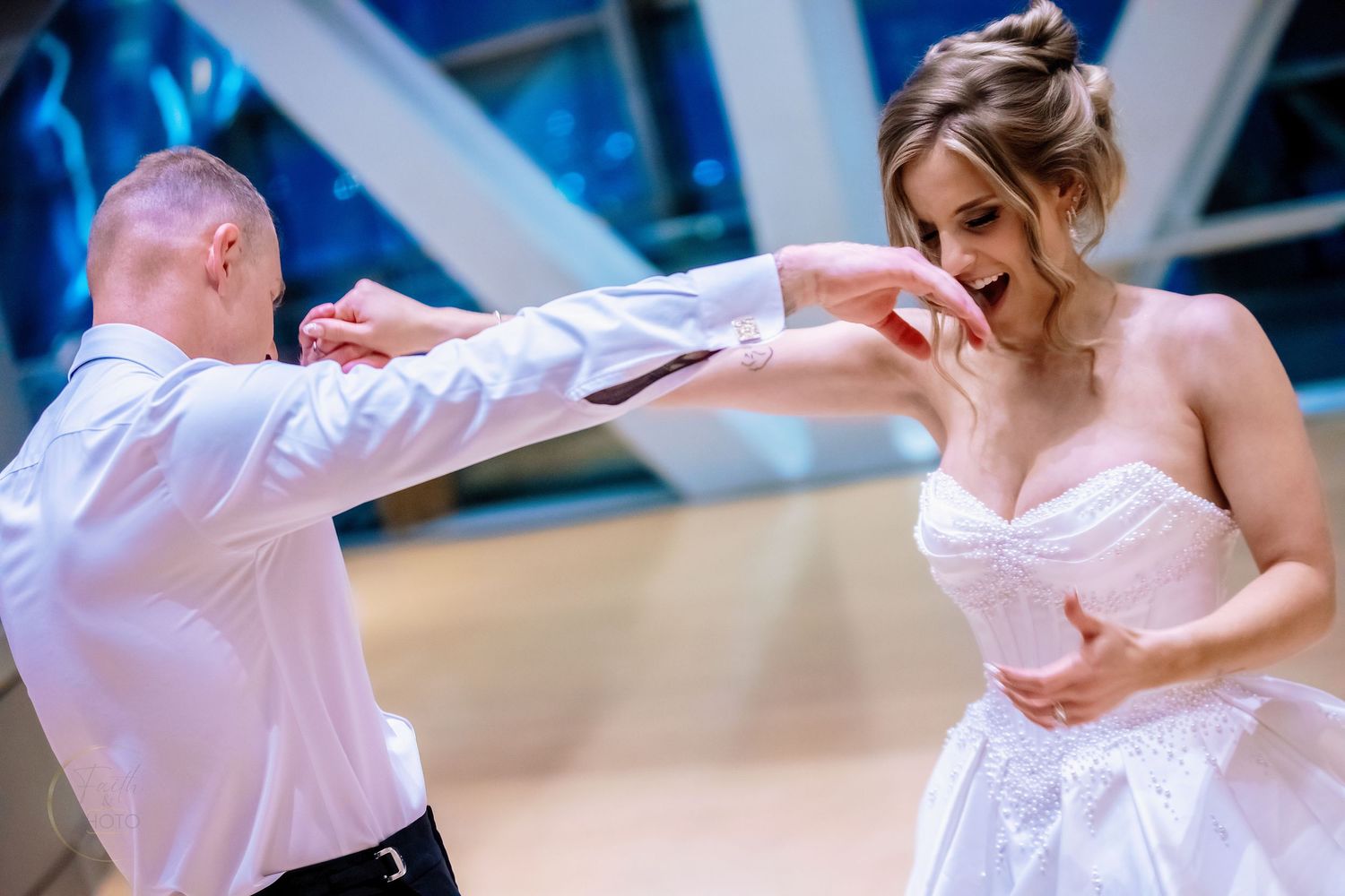 A bride and groom share a joyful first dance at their wedding reception, dressed in white formal attire.