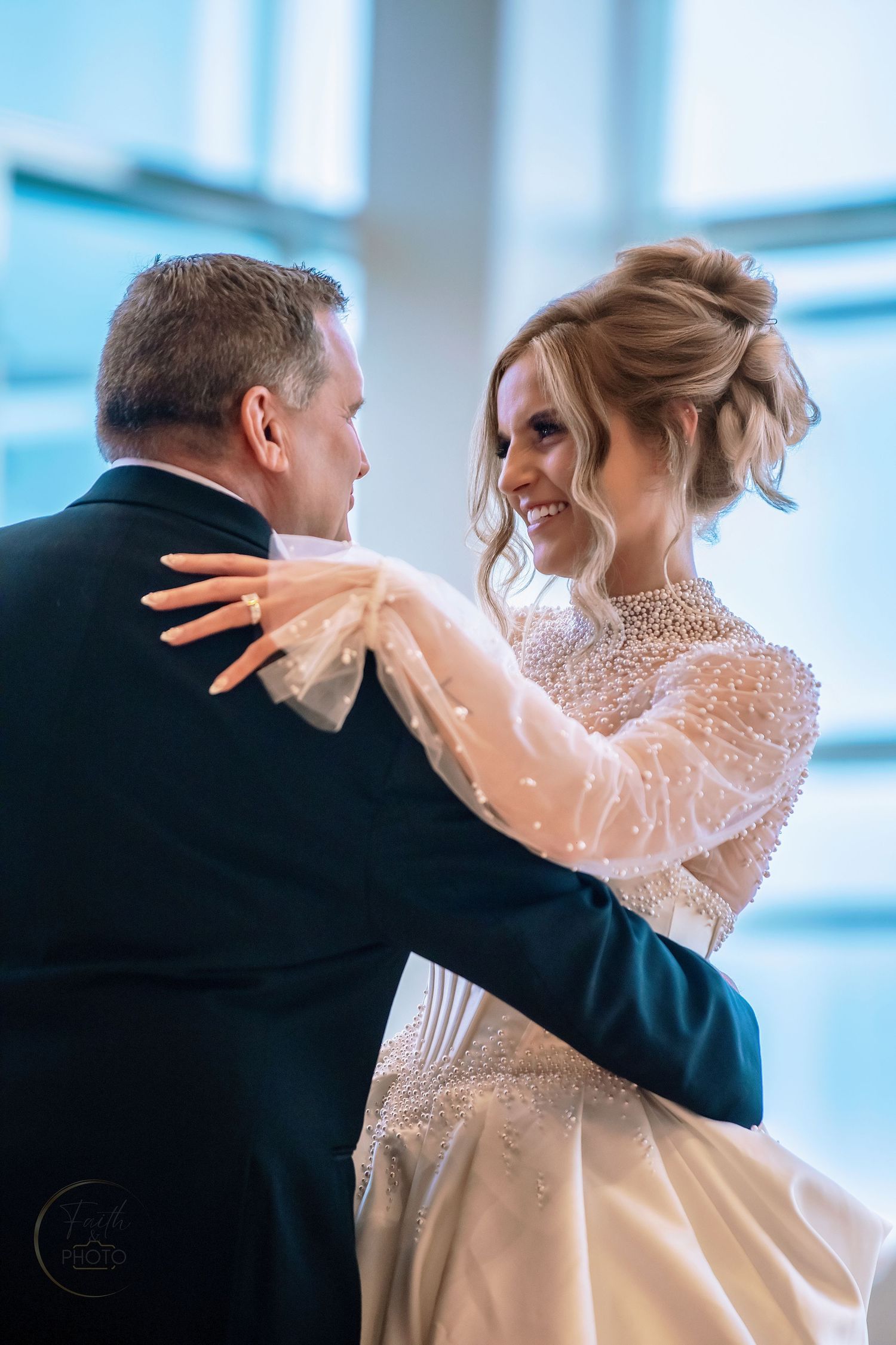 Bride and groom share their first dance, smiling at each other, bride wearing a beaded long-sleeve wedding gown.