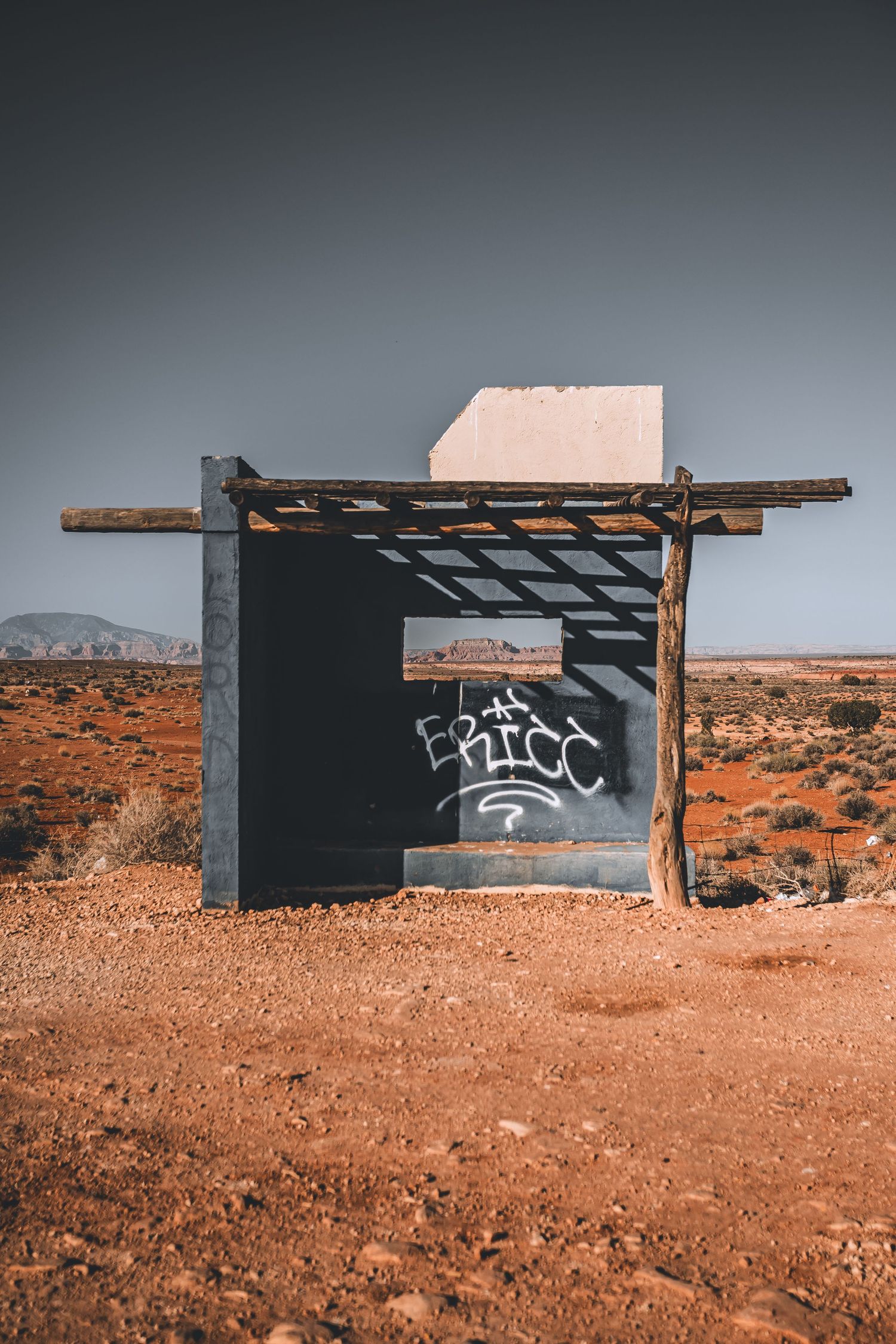 Abandoned desert structure with wooden beams and black walls stands against arid landscape and distant mountains.